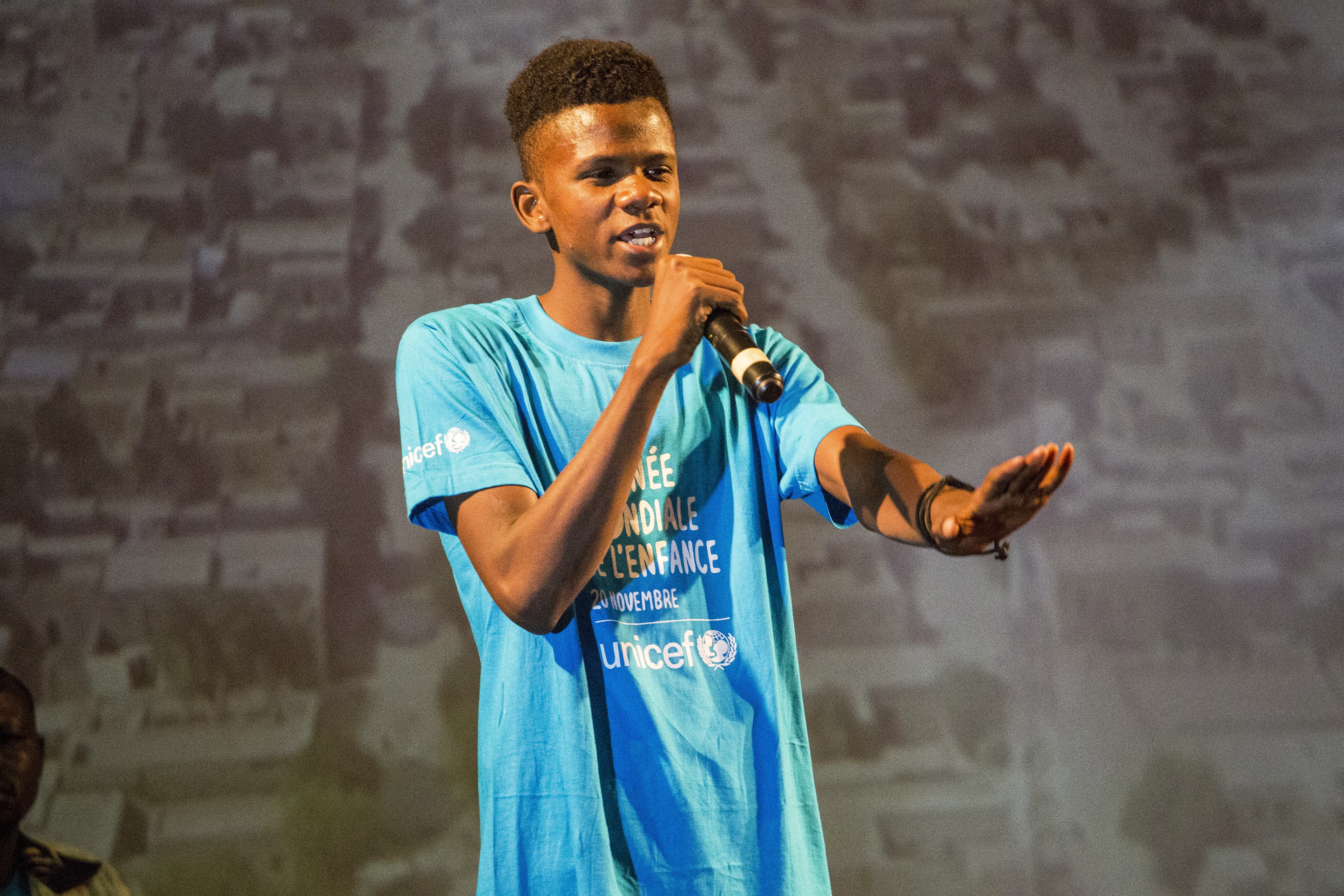 Teen boy holding microphone where World Children's Day cyan blue shirt