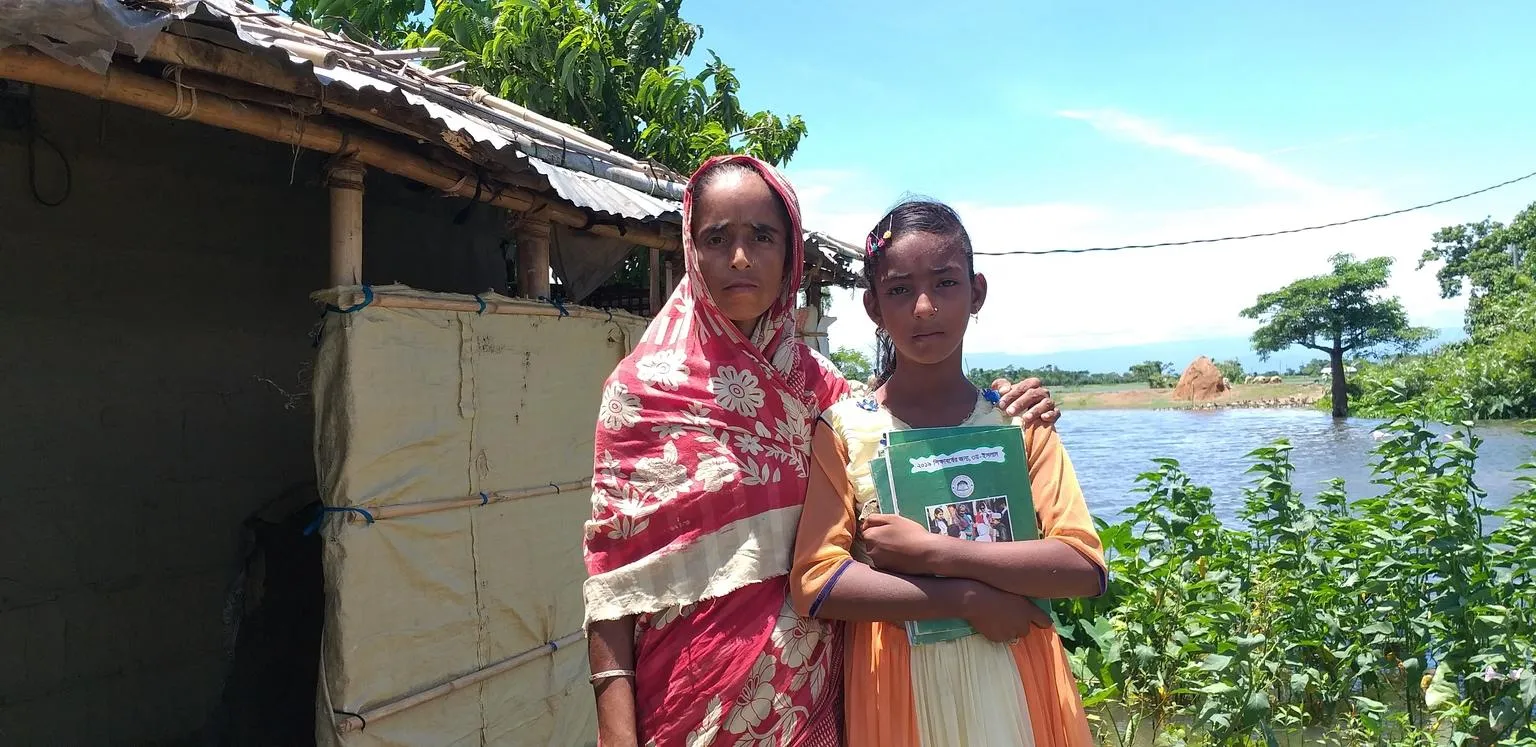 A woman and her daughter stand outside a makeshift home in Bangladesh.