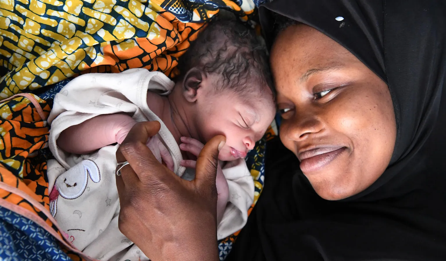 A women looks at her new born child smiling, the child's eyes are closed. This photo was taken in Odienné, in the Northeast of Côte d'Ivoire 