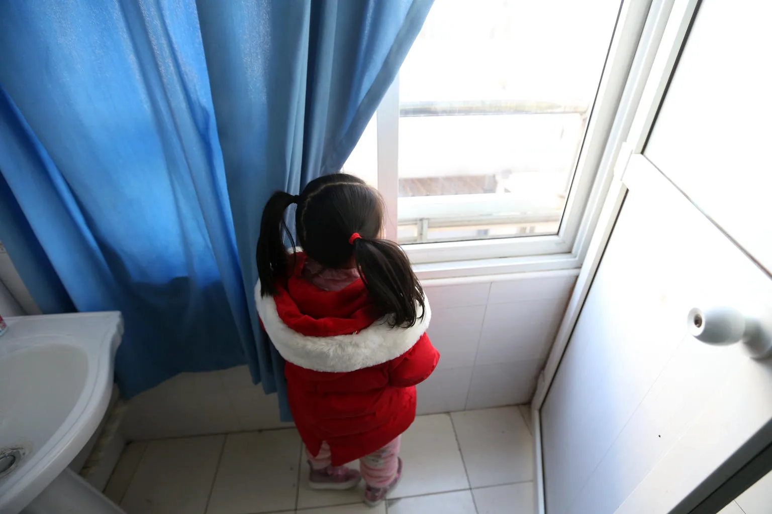 A little girl looks out a hospital window where she is being cared for while her family undergoes treatment for COVID19.