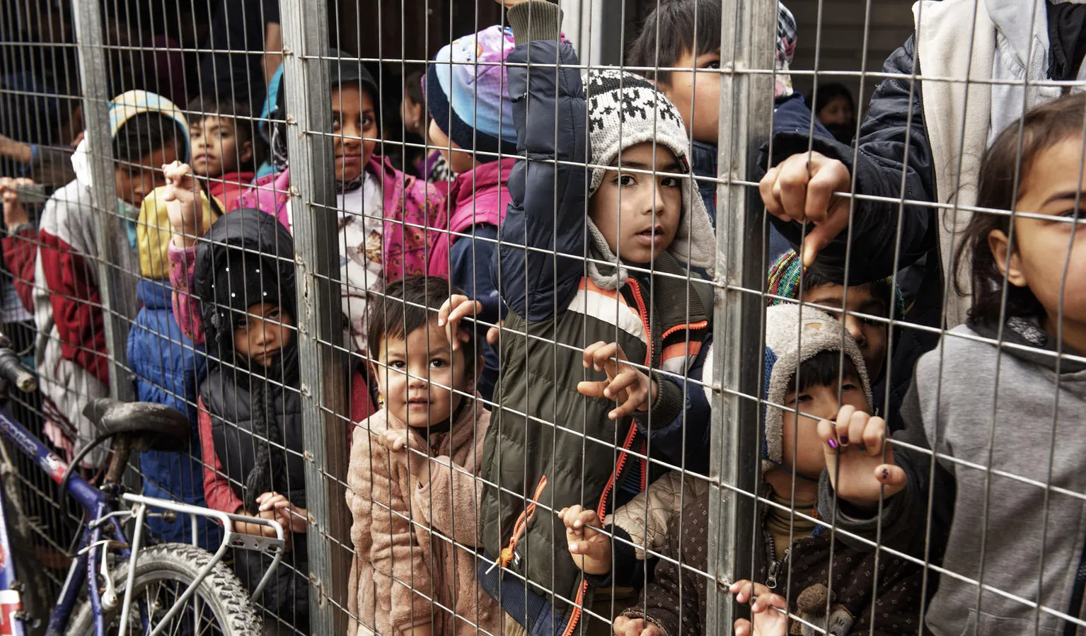 Children wait in a crowded processing area for refugees.