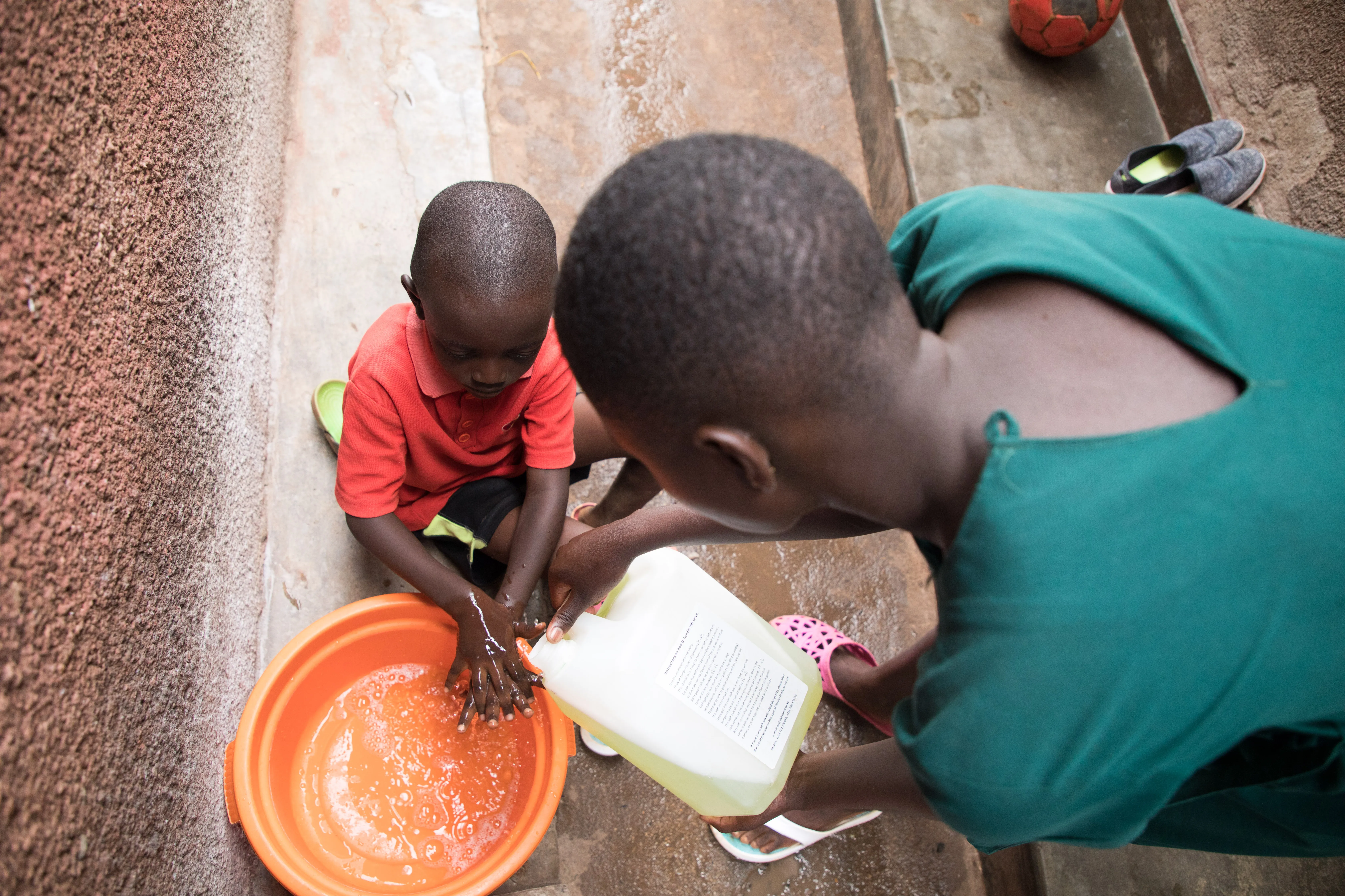 Sharon helps Jonathan to wash his hands with the water and soap mixture at the entrance of their house. In Uganda, the COVID-19 pandemic and lock down has left many families with no option but to stay home and keep stay safe. 