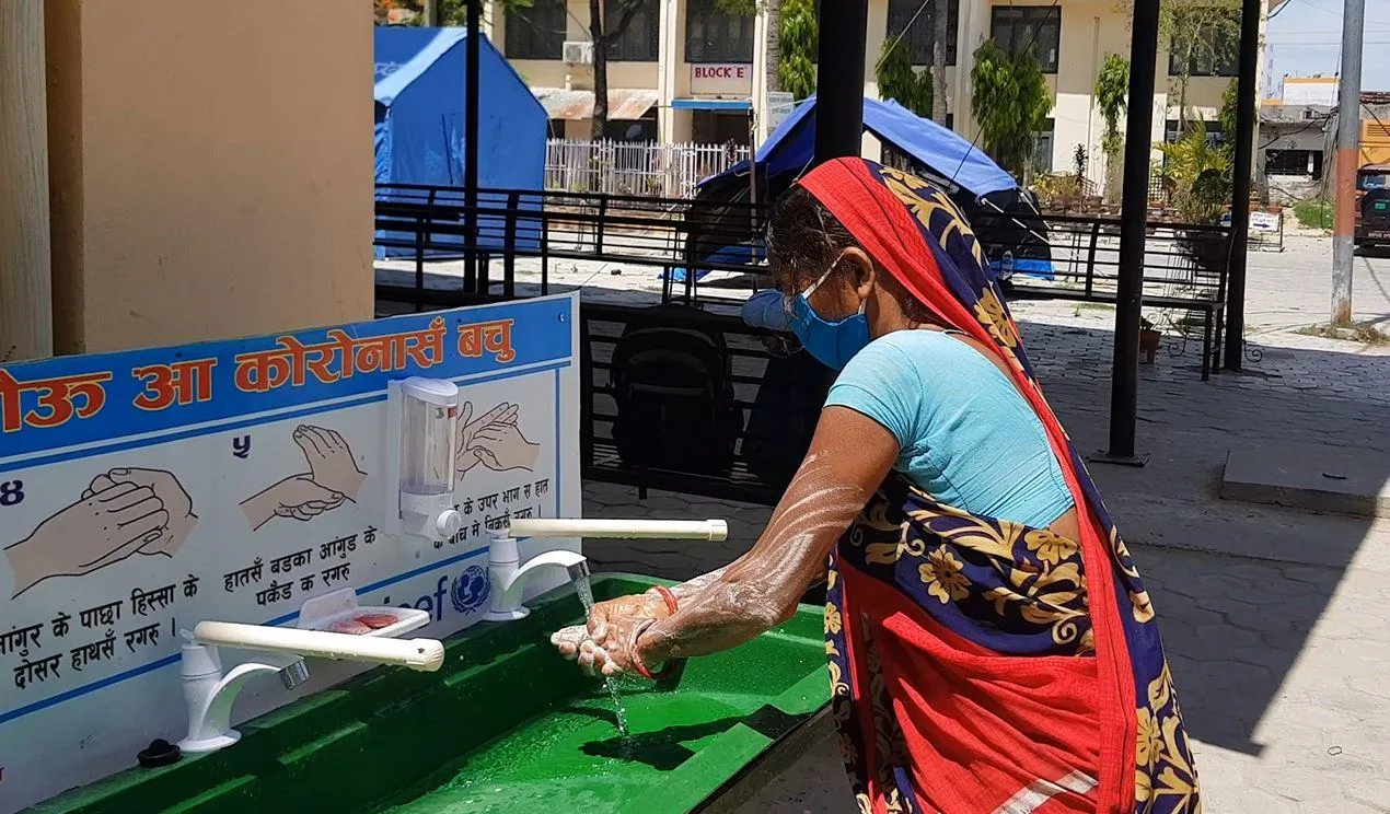A woman washes her hands at a portable washing station.