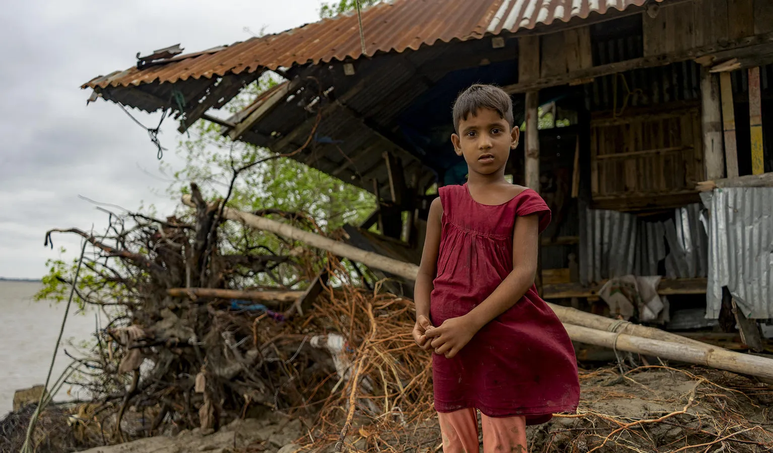 A child stands in front of her tin house in Bangladesh.