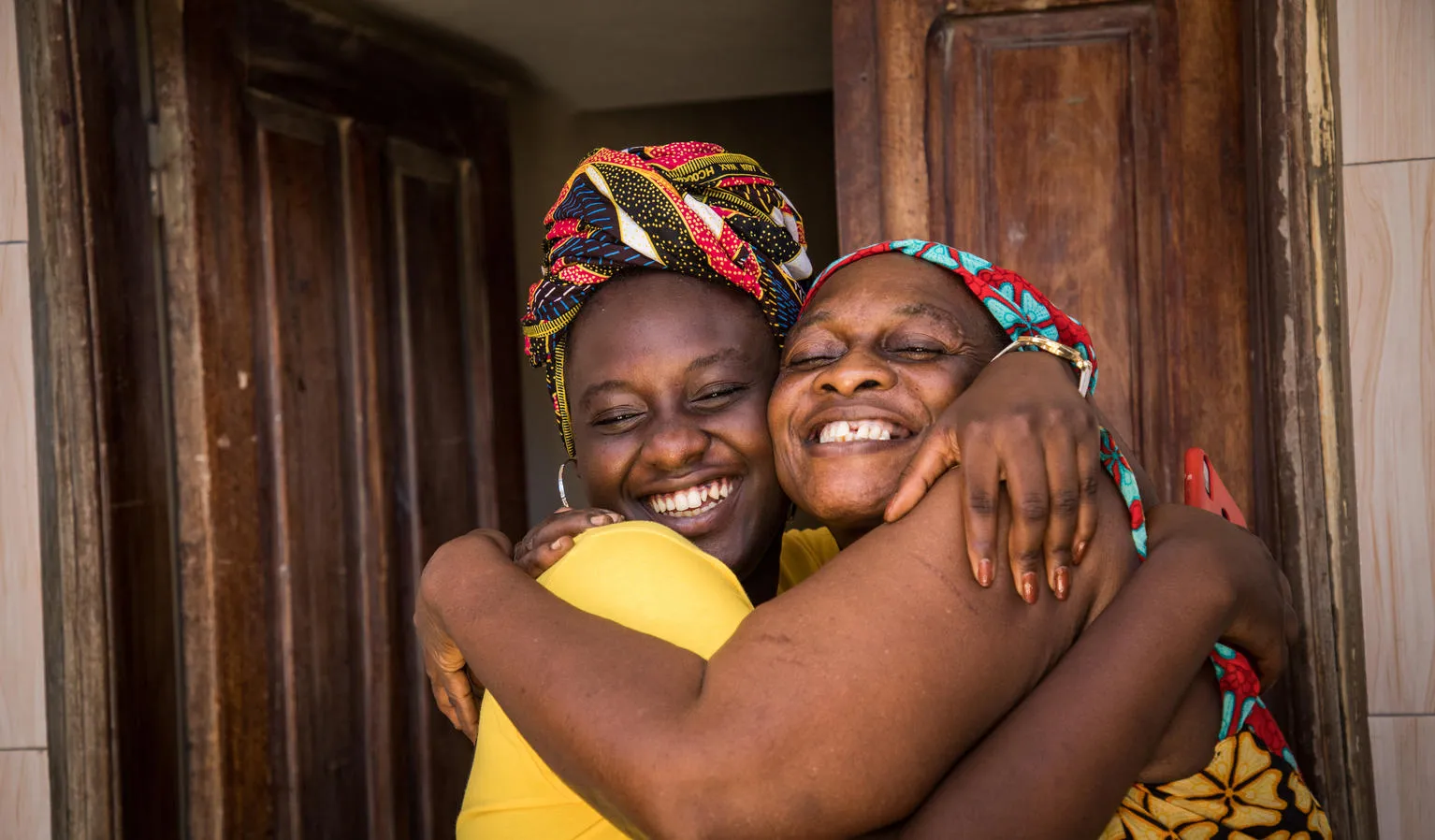 A mother and daughter hug outside their home.