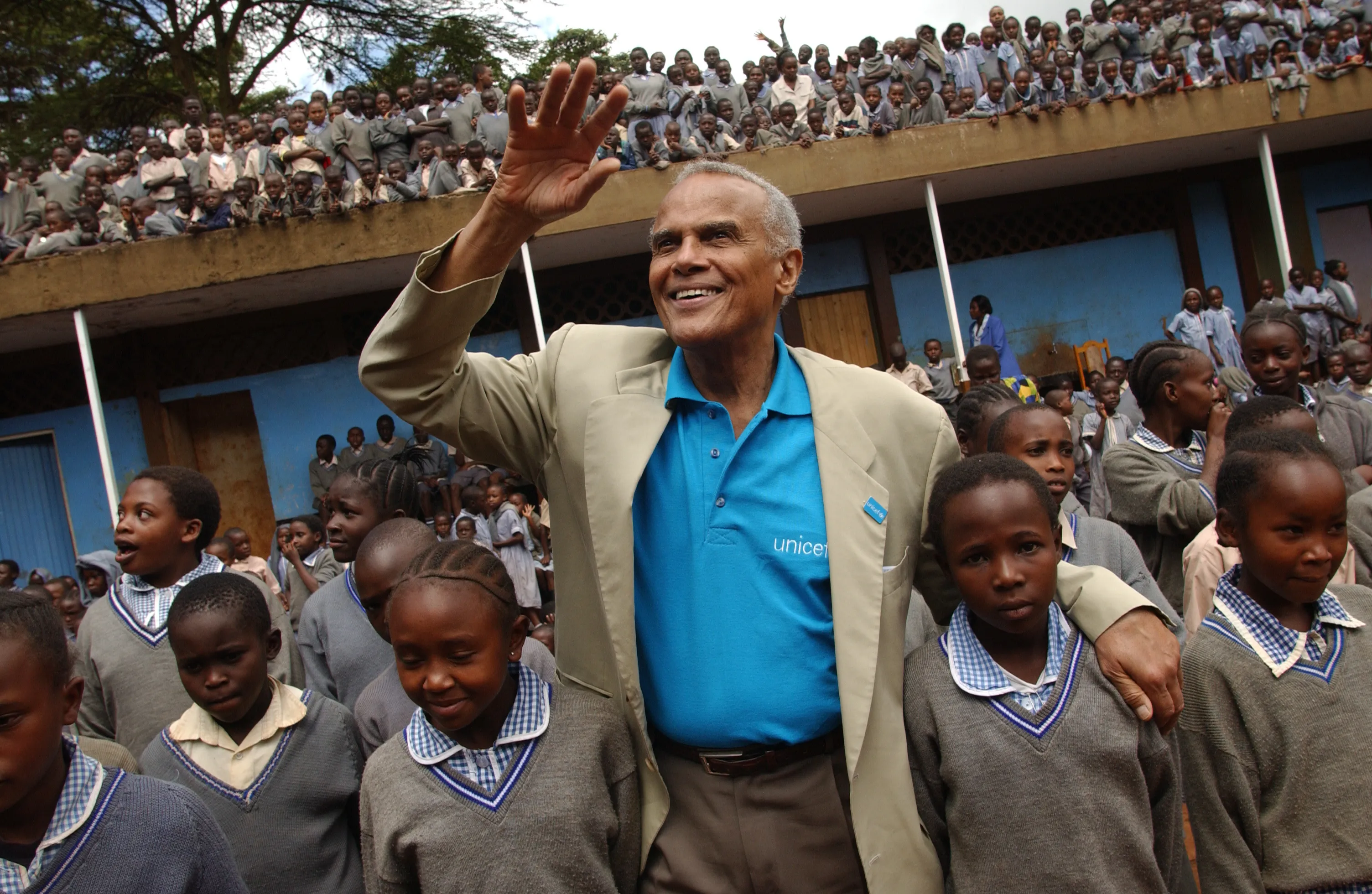 UNICEF Goodwill Ambassador Harry Belafonte waves to onlookers, standing amidst a crowd of children at the Kihumbuini primary school in Kangemi, a poor neighbourhood in Nairobi, the capital.