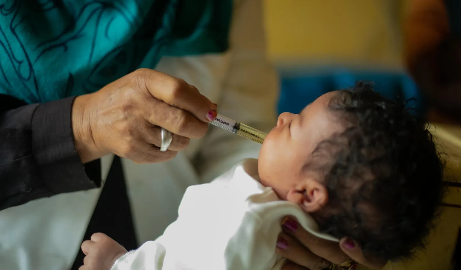 A hand administers a vaccine to a baby, using a plastic syringe.