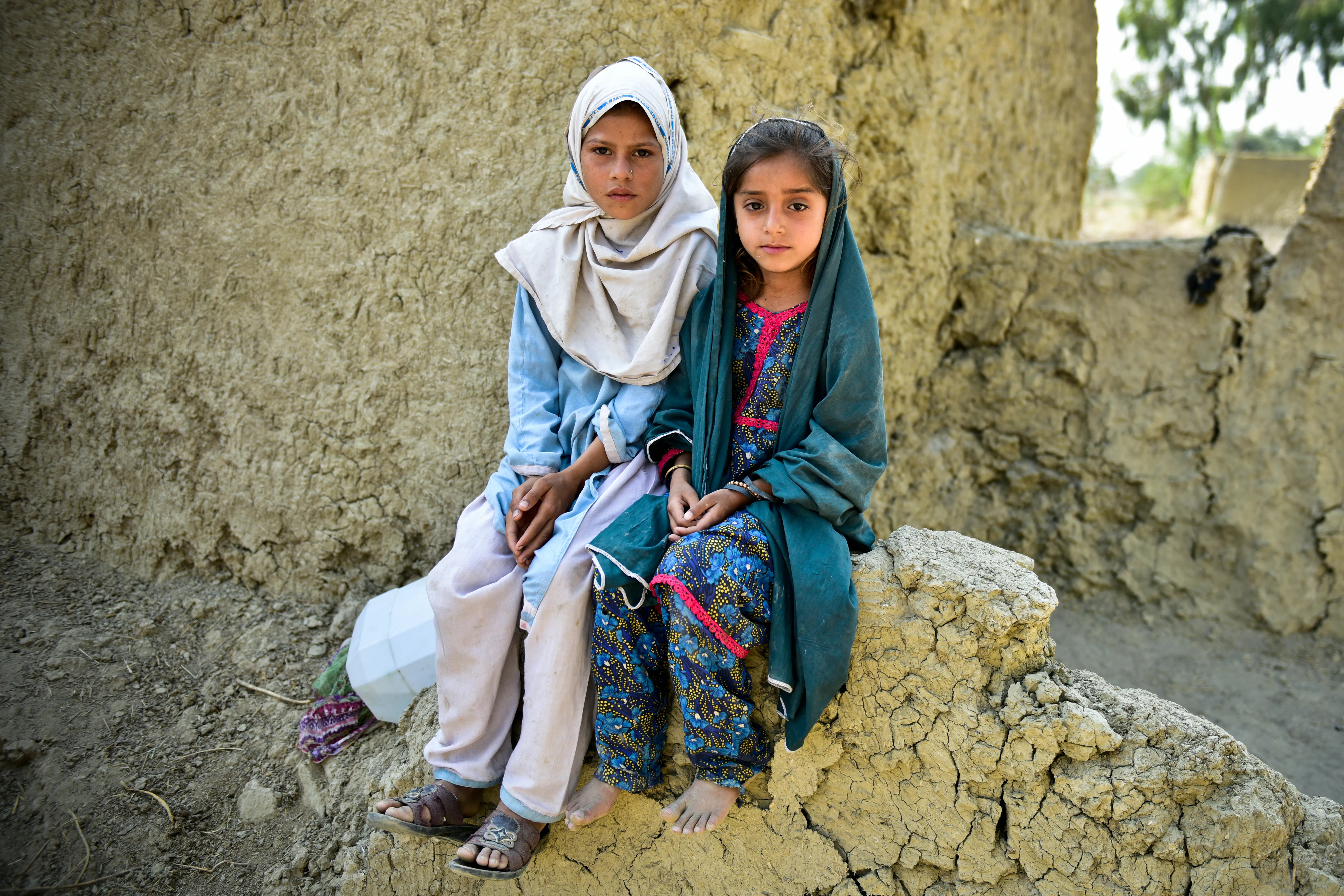 Muriko bibi (7) and Tehseen (6) sit on the damaged wall of their mud house which was almost destroyed during the 2022 floods in Pakistan.