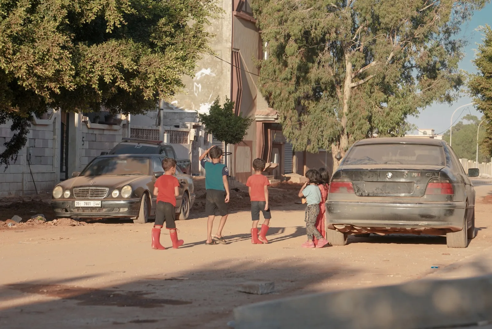 Young children are walking around in the neighborhood in boots despite the hot weather because they still worry about the floods and drowning, they have been displaced to a whole new city that they are still trying to familiarize themselves with.