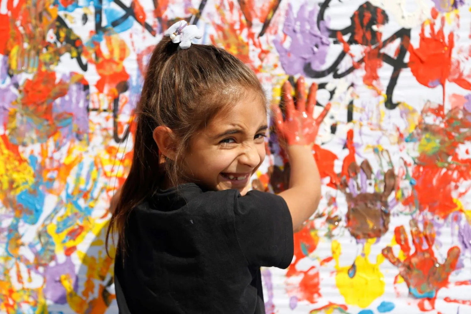 Dans un centre soutenu par l’UNICEF en Türkiye, une fille souriante pose ses mains couvertes de peinture sur un mur d’empreintes colorées.