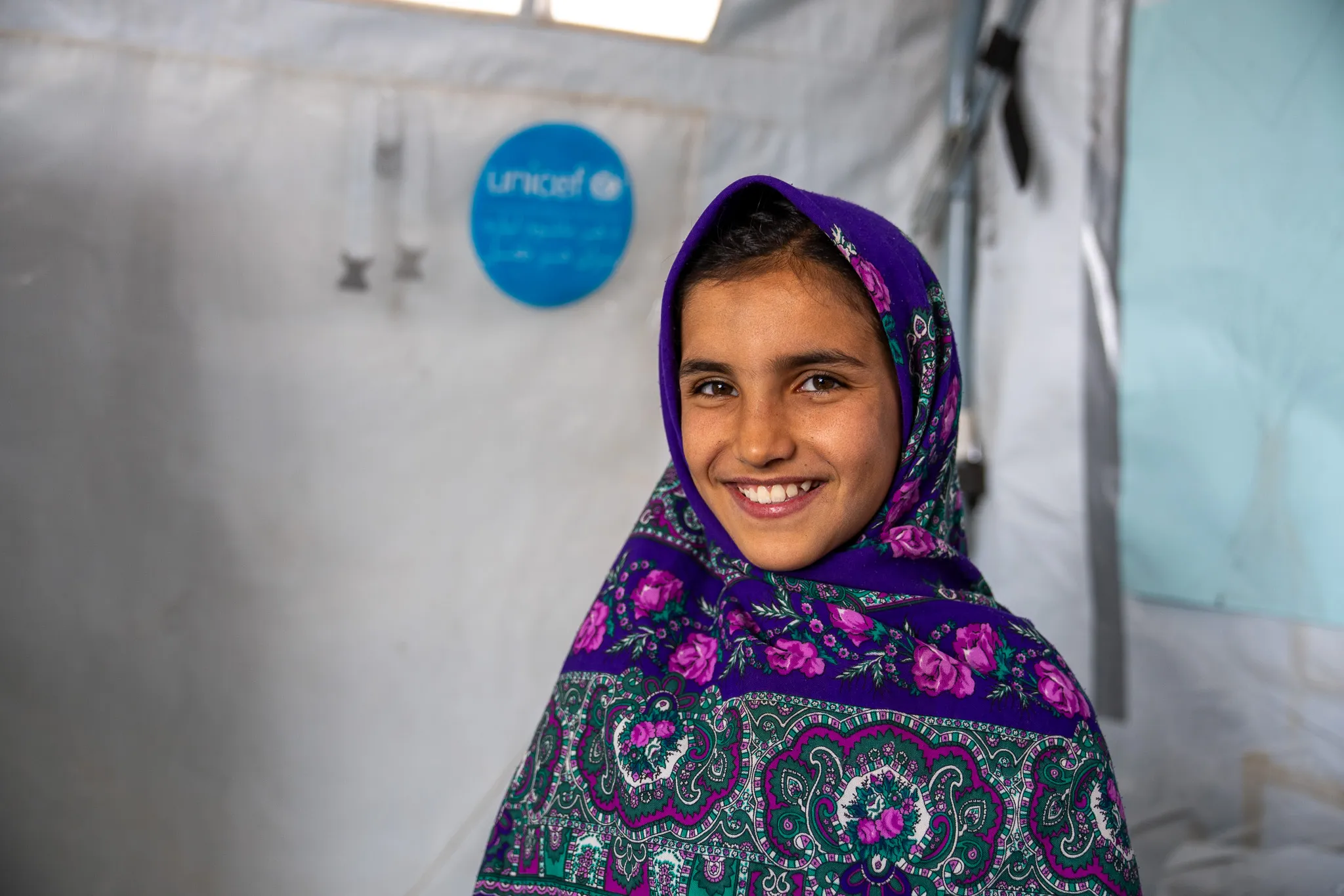 Girl in a headscarf smiling inside a UNICEF-supported learning space in Herat, Afghanistan.
