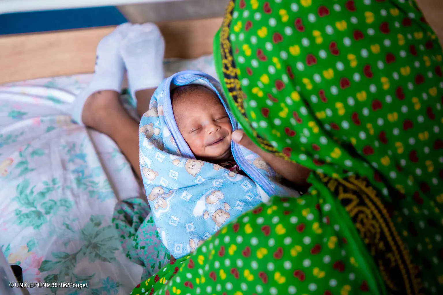 Un bébé enveloppé dans une serviette sourit sur les genoux de sa mère.
