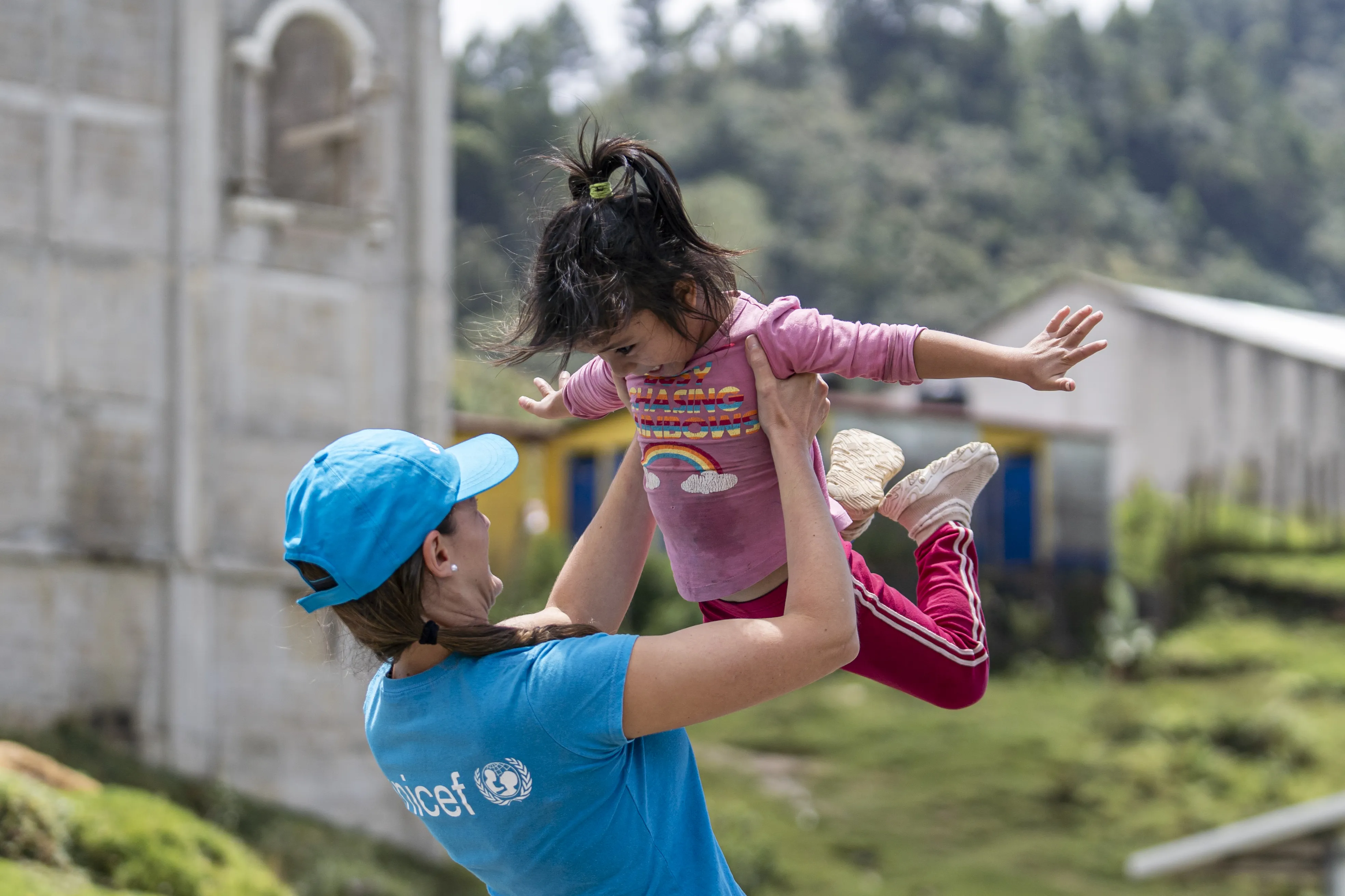 A woman, a UNICEF Staff member, raises a child high above her head, capturing a delightful moment of connection and joy in their interaction.