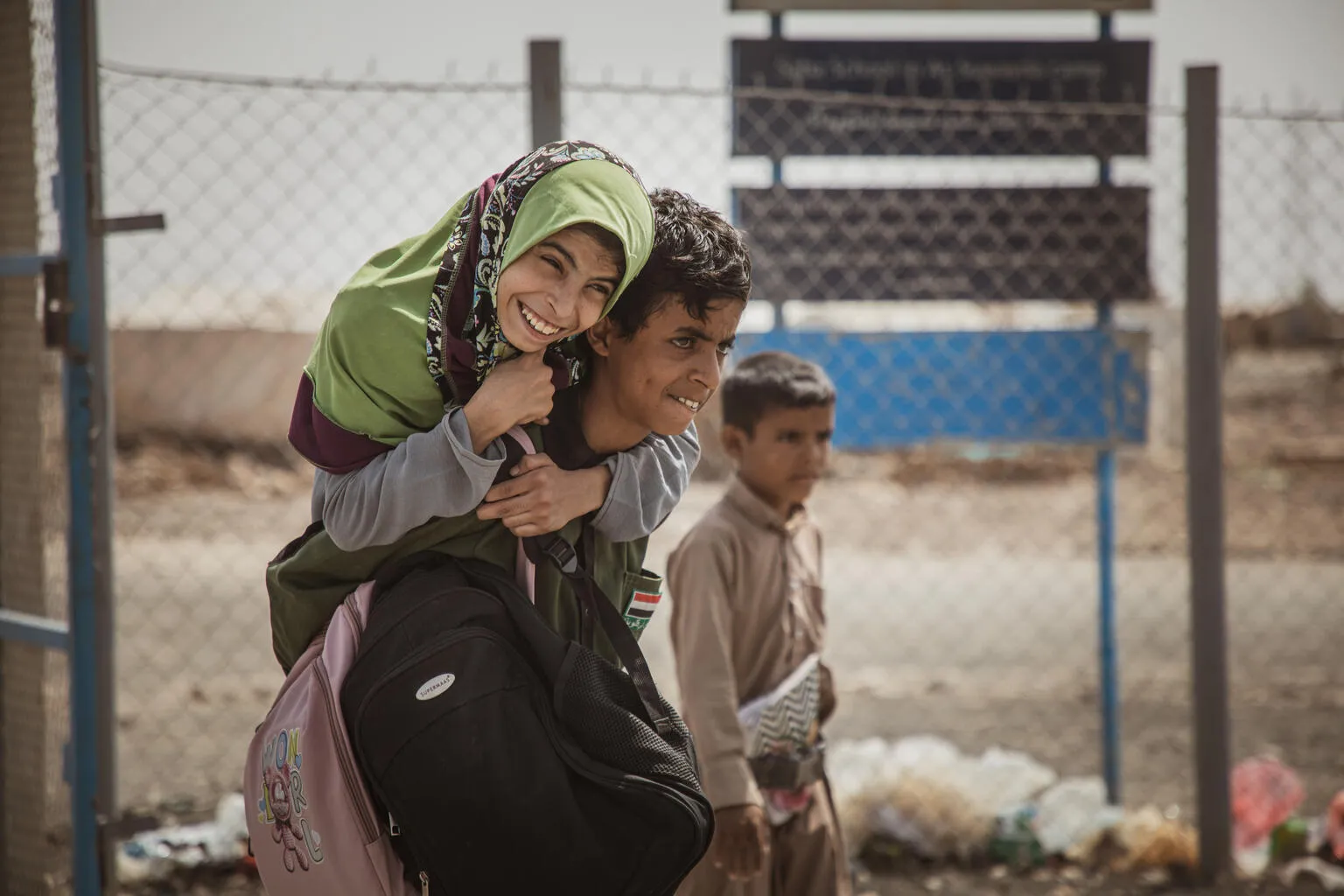 In Yemen, a boy carries a smiling girl wearing a green headscarf on his back. 