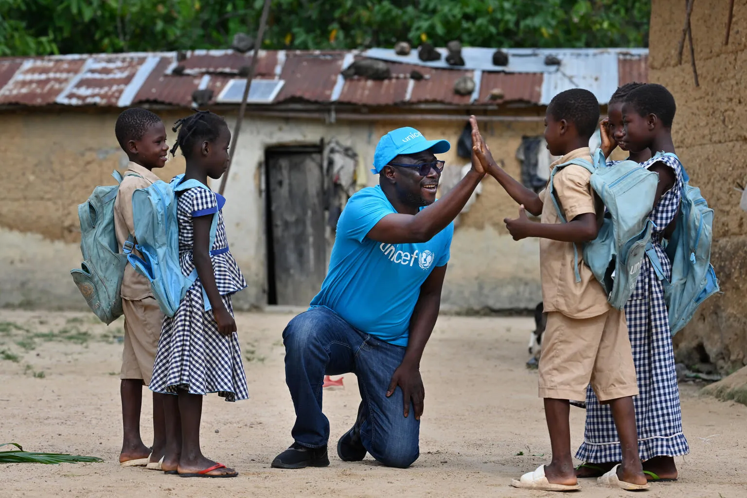 Un employé de l’UNICEF tape dans la main d’un jeune garçon tandis que d’autres enfants se tiennent autour d’eux.