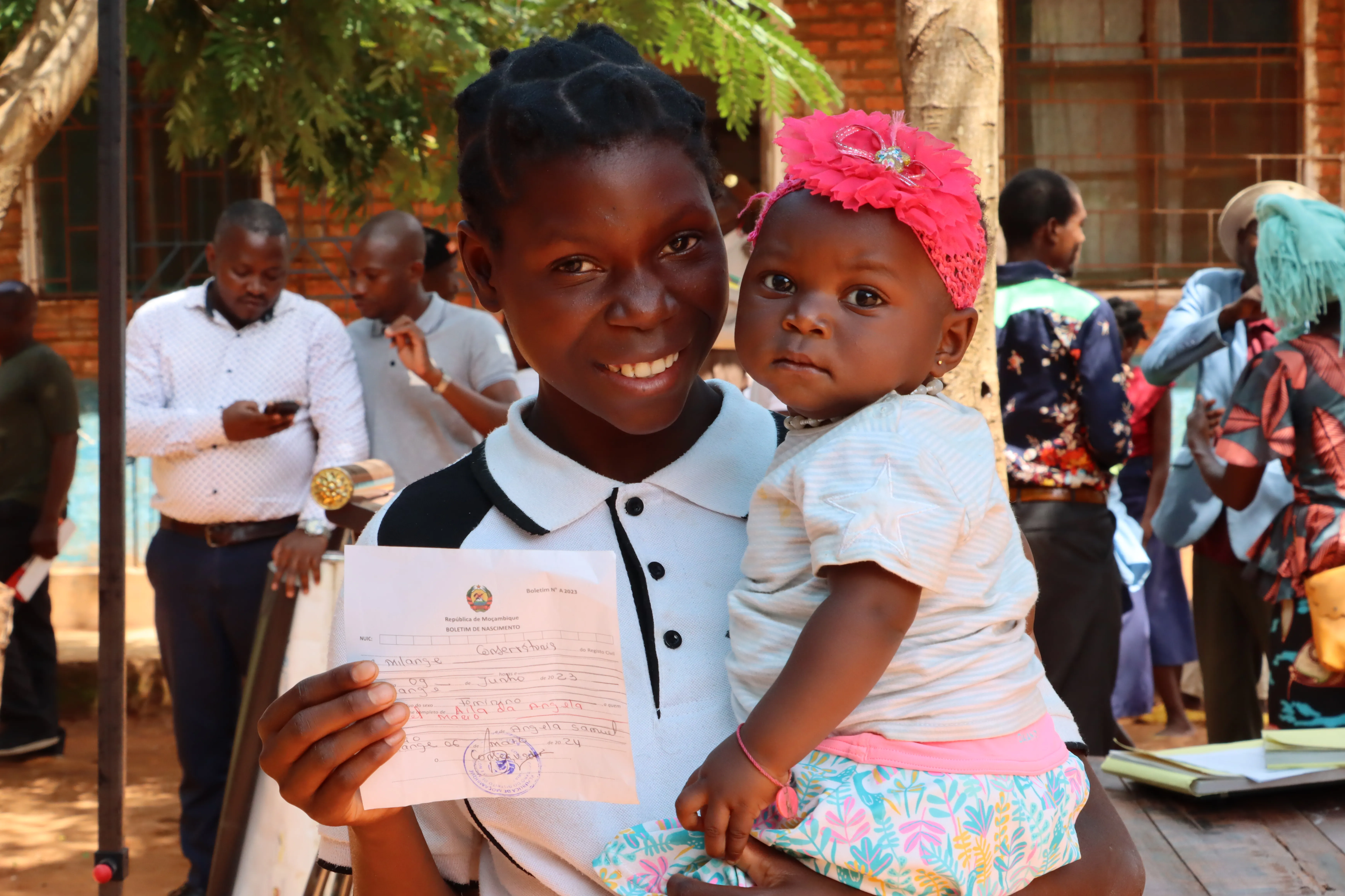 A mother holds her child lovingly while also showing the child's birth registration certificate. 
