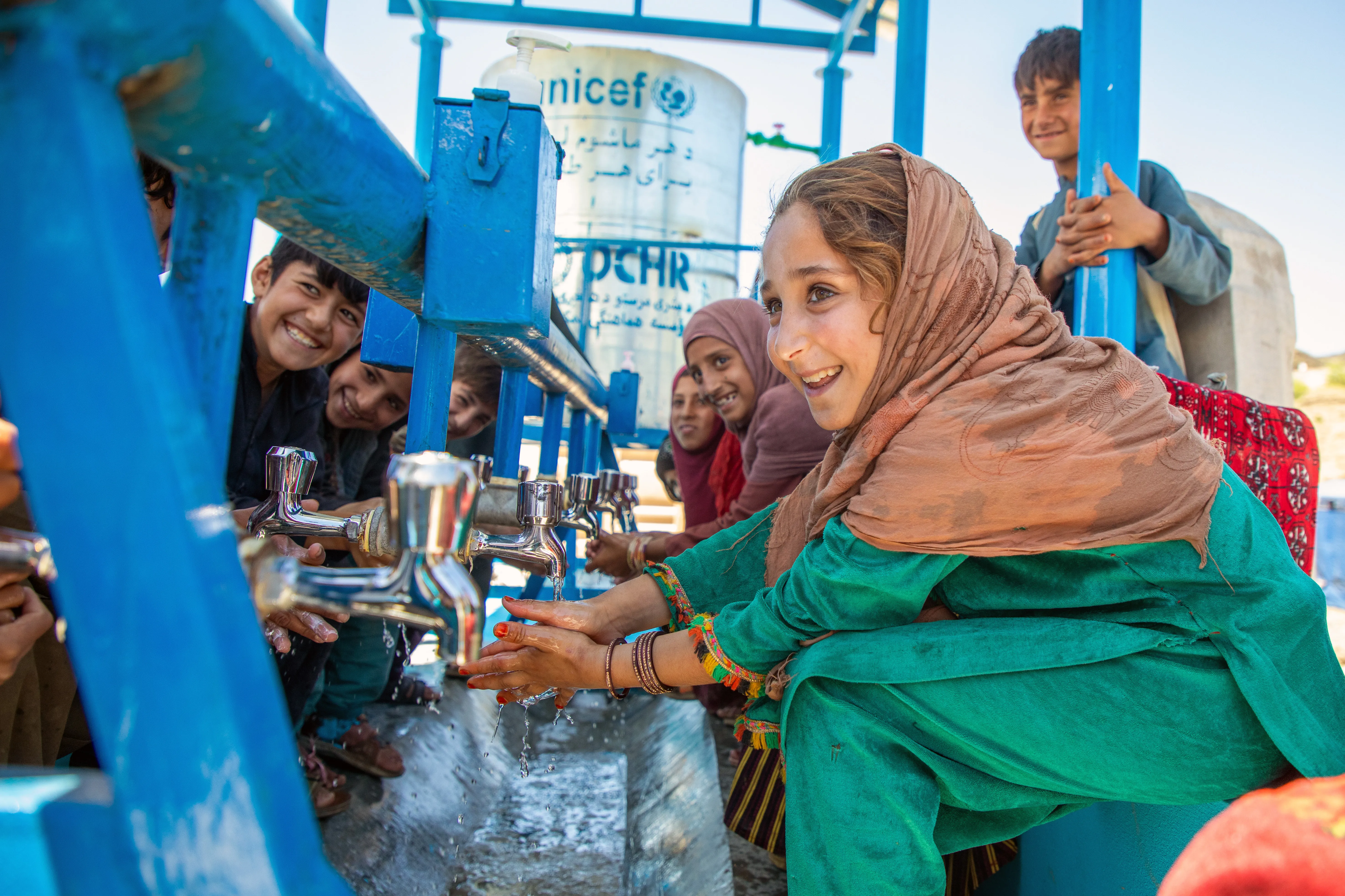 A 9-year-old girl washes her hands with water from a tap.