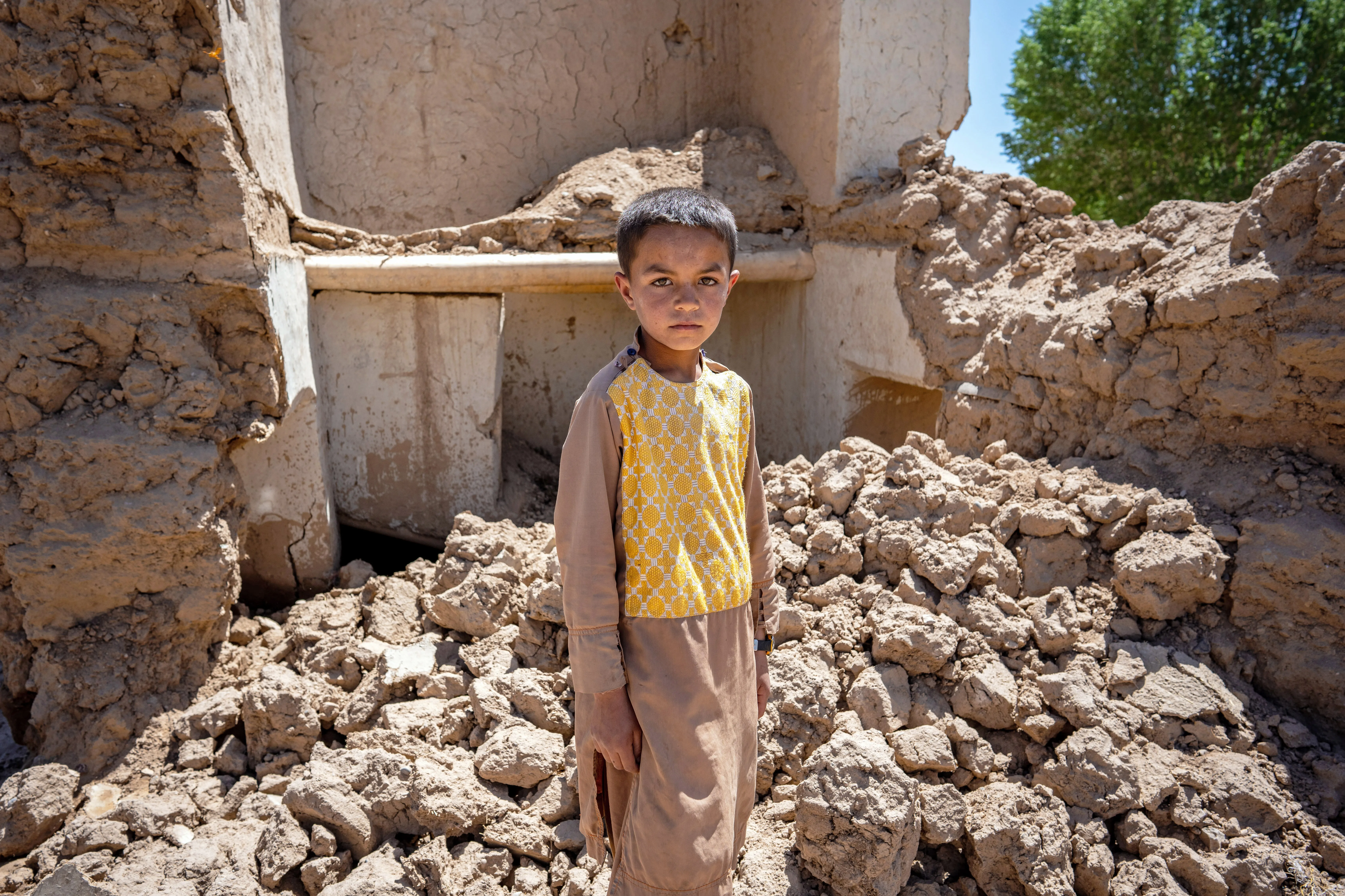On the 28th May 2024, 9 year old Farzan is photographed in the ruins of his house in Chaghcharan district, Ghor province in western Afghanistan.