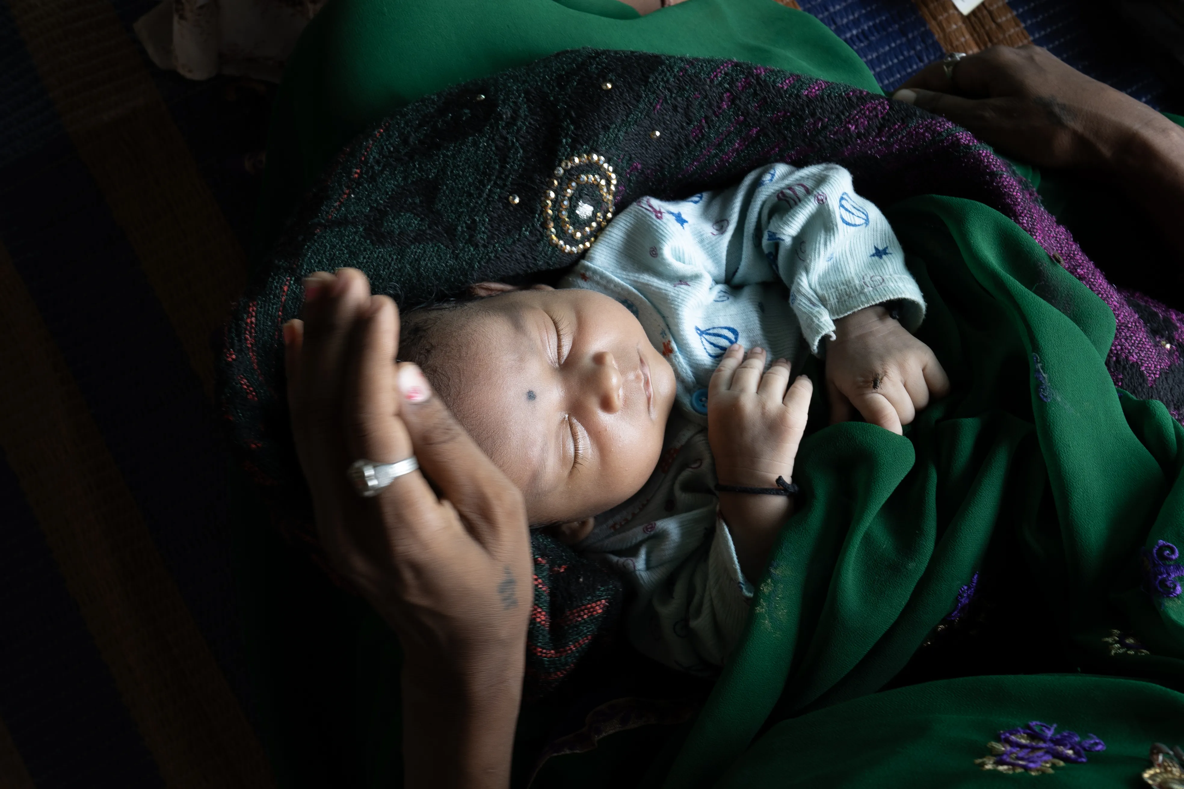A newborn sleeps in their mother's lap in a HBPNC (Home-based postnatal care) in Balolabadi, Jhabhua, Madhya Pradesh, India. 