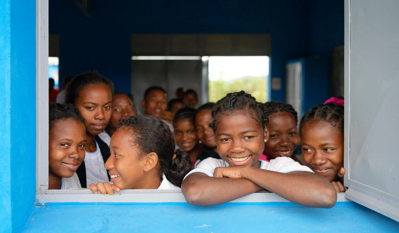 A group of young girls smile and look out from a window.