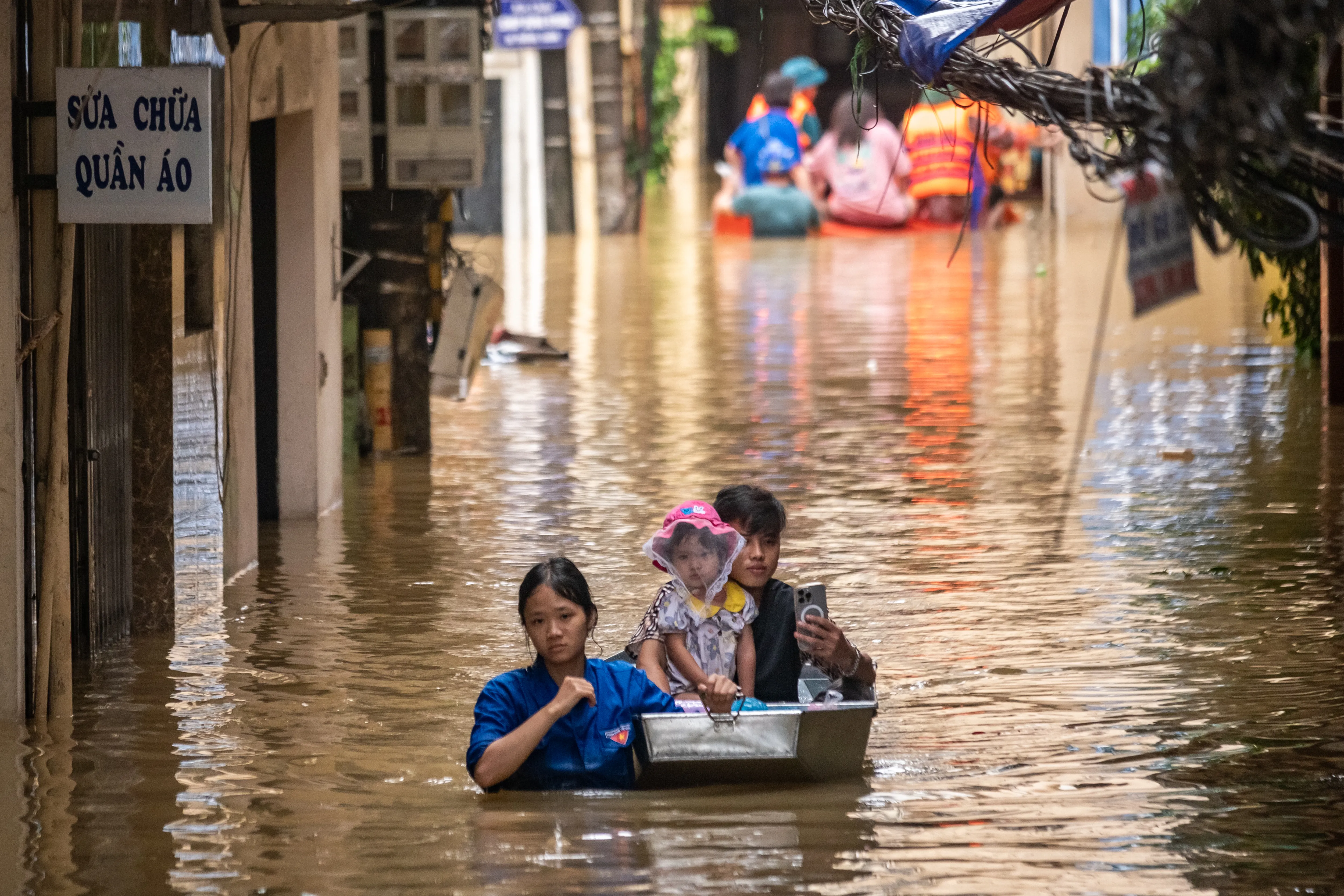  A woman, a man and child navigate a flooded street, showcasing the impact of heavy rainfall on their surroundings.