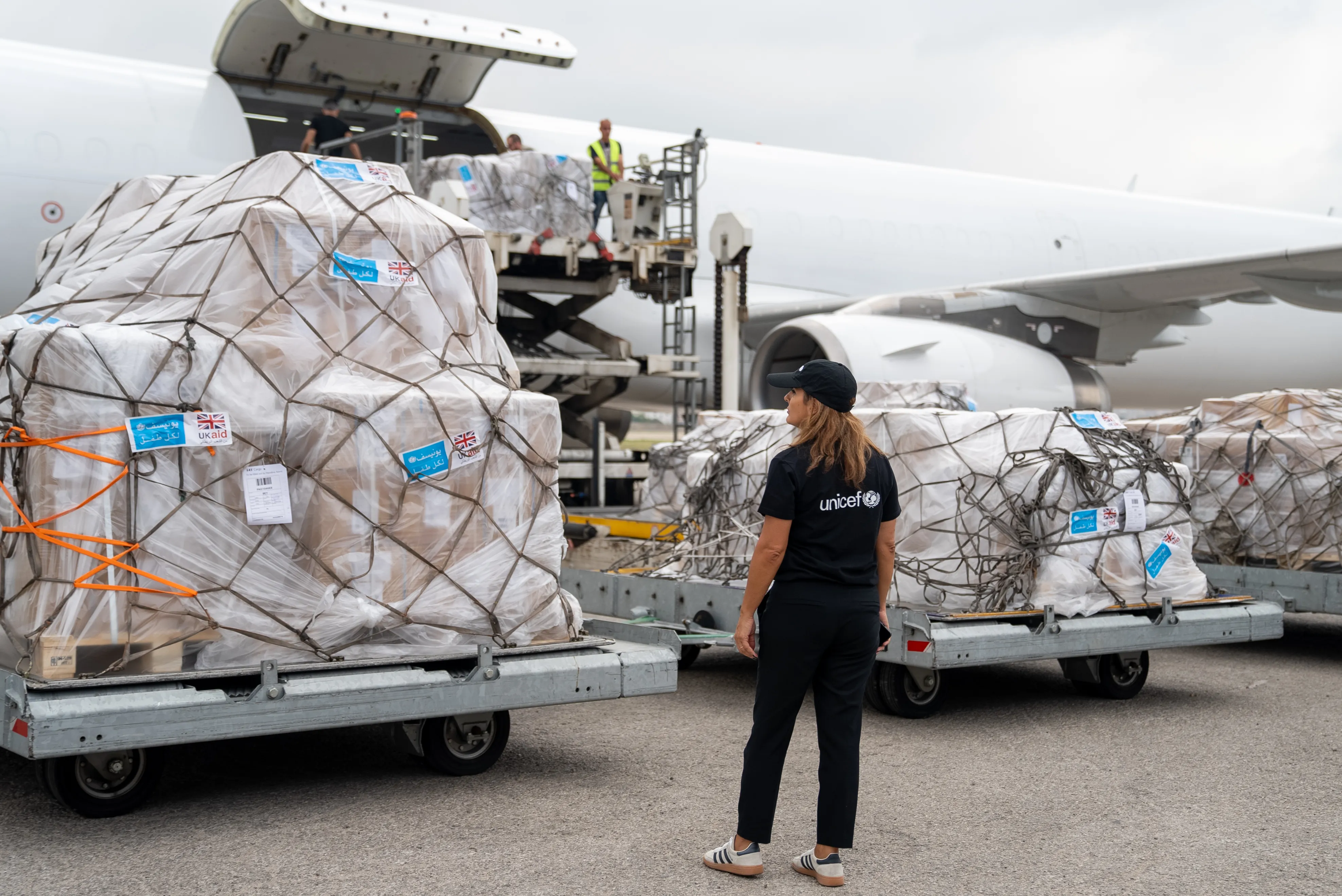 A UNICEF worker oversees humanitarian aid being offloaded from a cargo airplane.