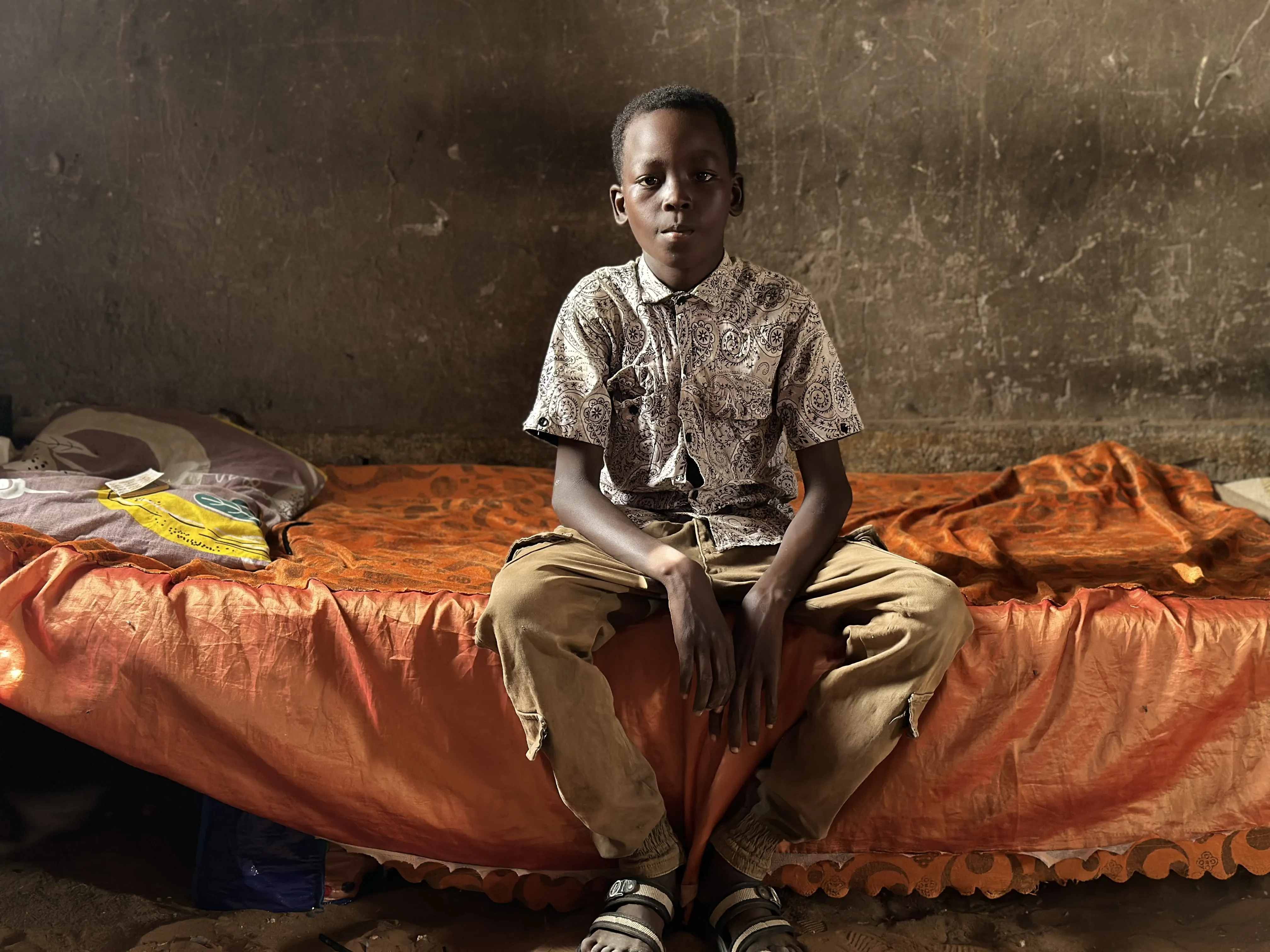 A boy sits in his home as he looks towards the camera in Sudan