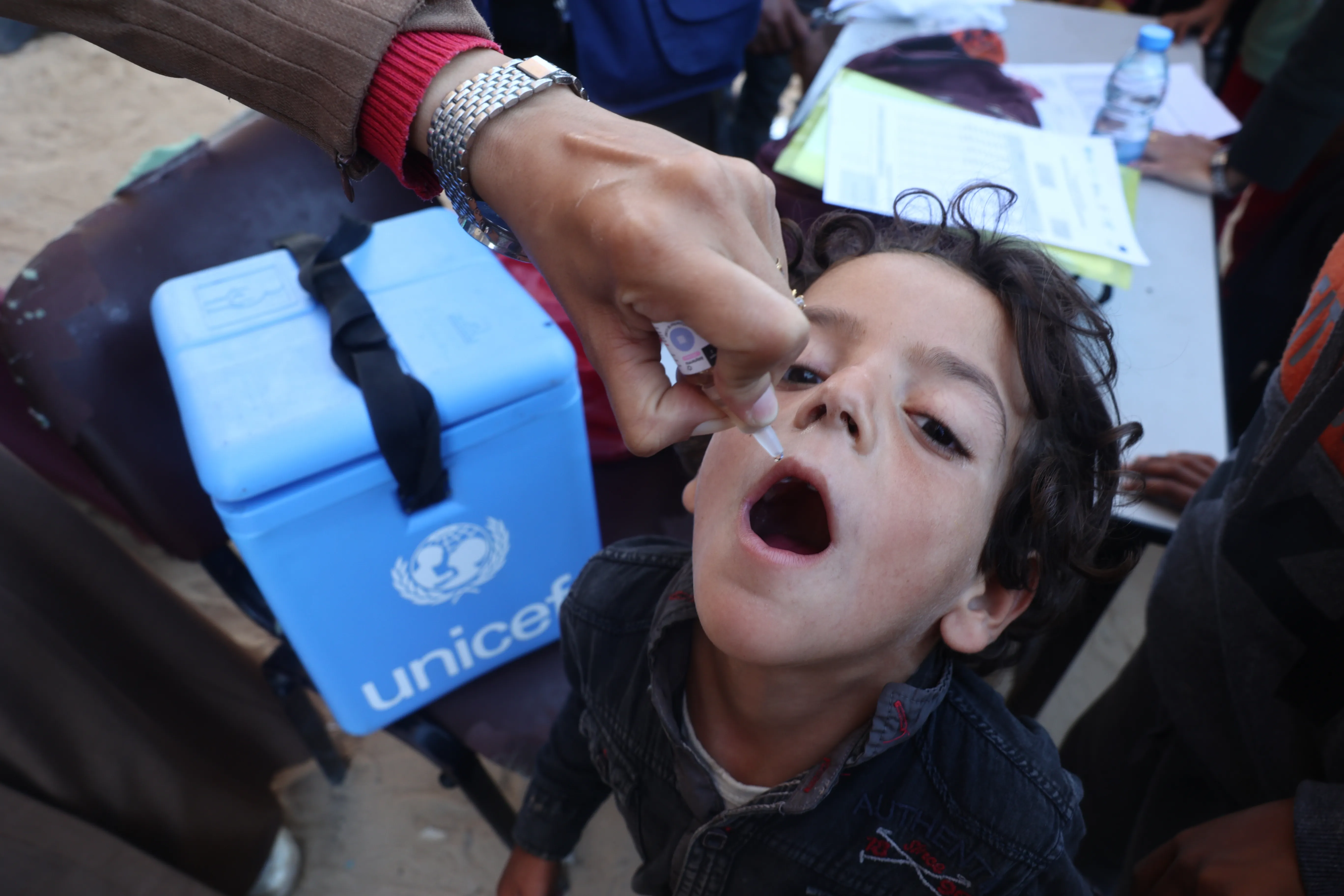 A child is being vaccinated while UNICEF's vaccination cold storage can been seen as well