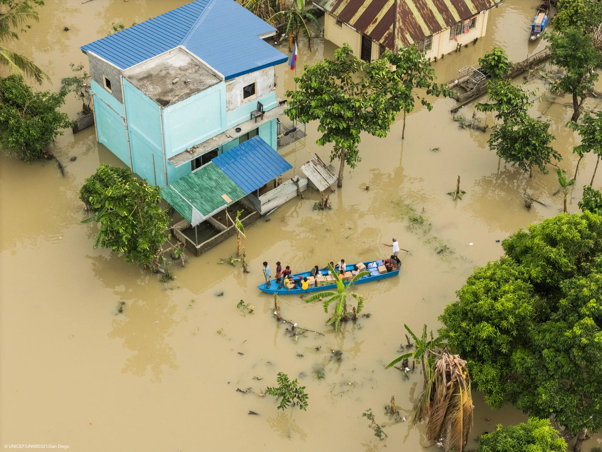  Individuals in a boat traversing a flooded street adjacent to a flooded house, highlighting the effects of severe flooding in the area.