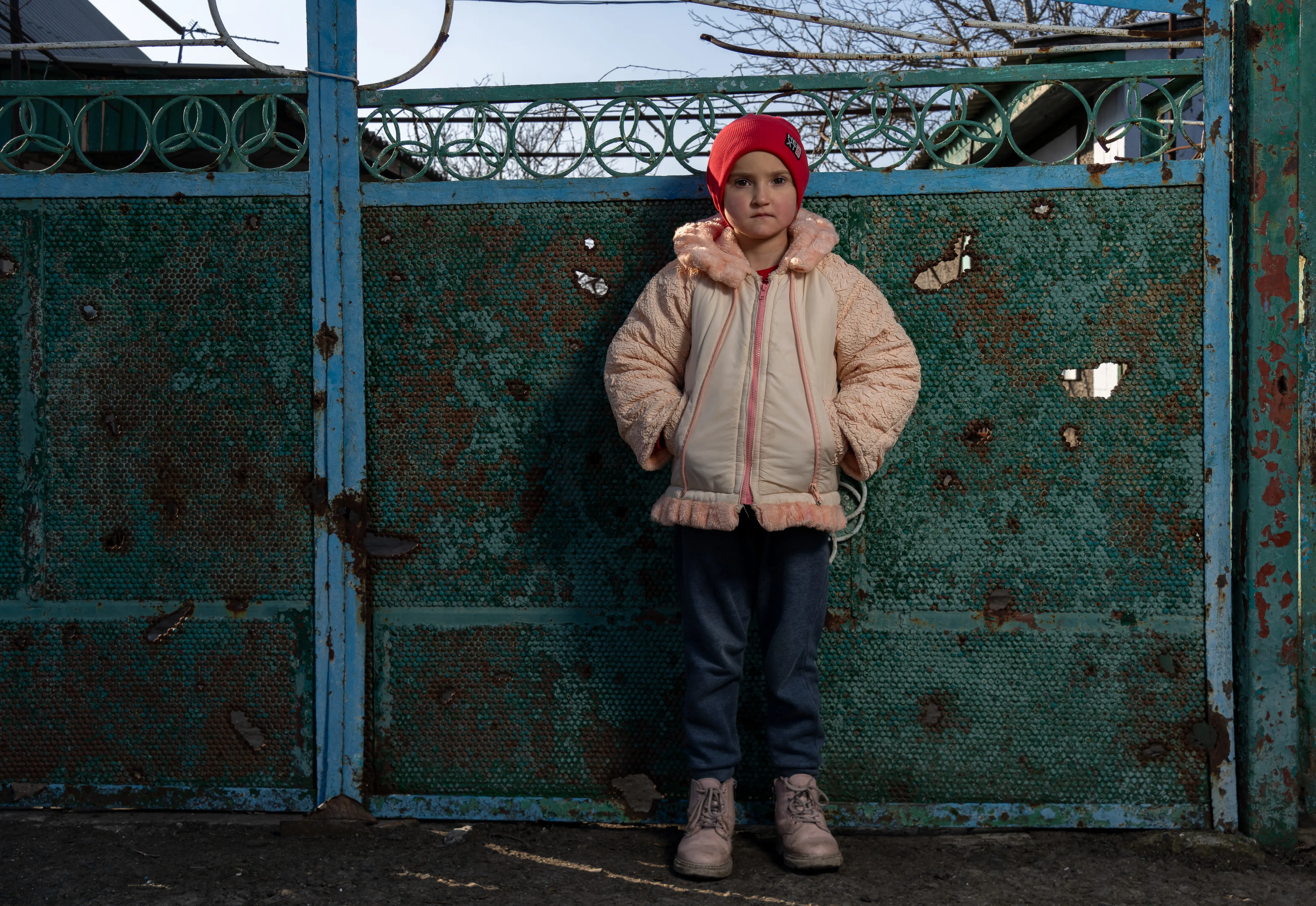 A Ukrainian child, looks towards the camera while wearing a winter jacket and red tuque.