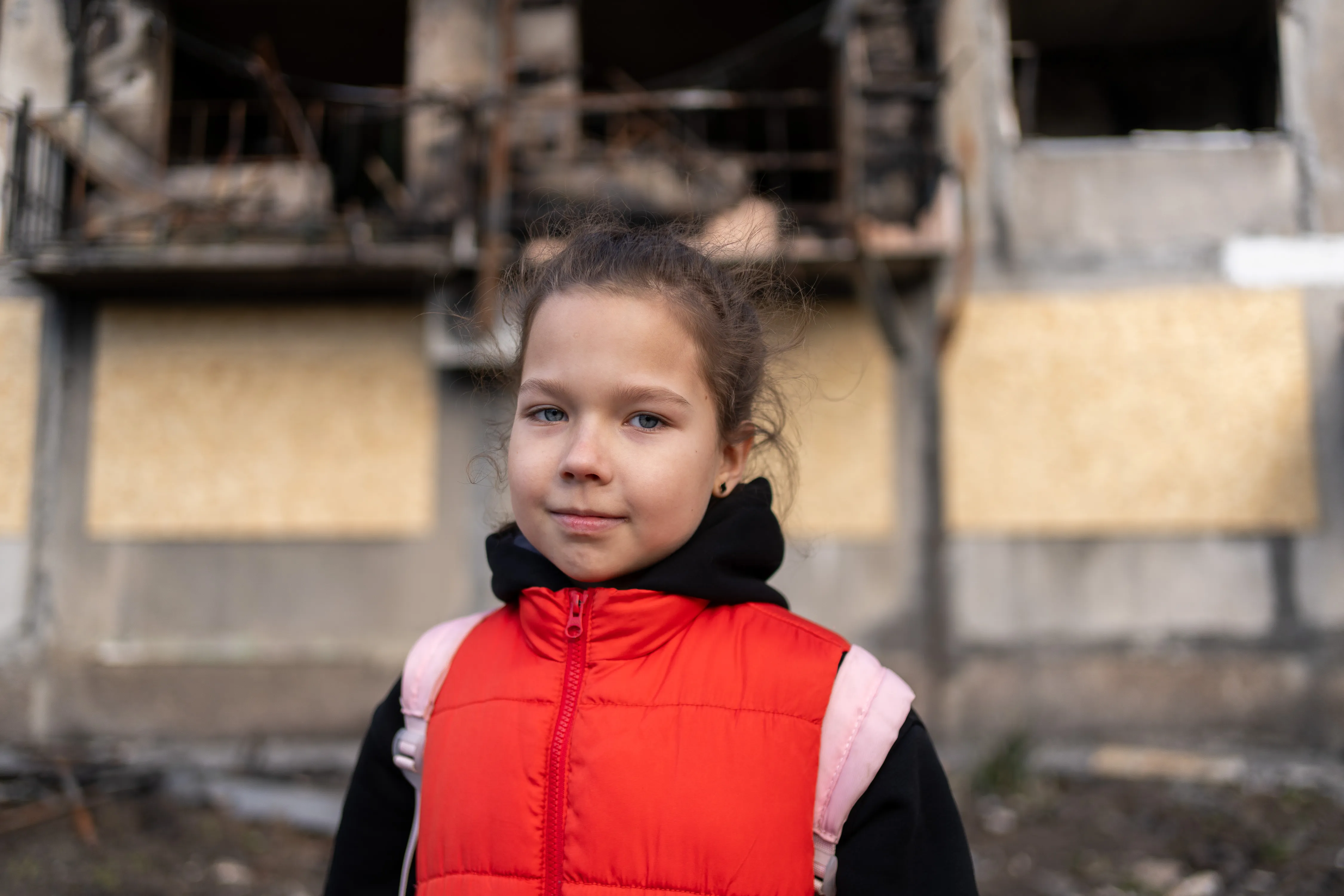 Eight-year-old Myroslava stands in front of a bombed-out residential building, one of several damaged in a missile strike on 7 March in Eastern Ukraine.