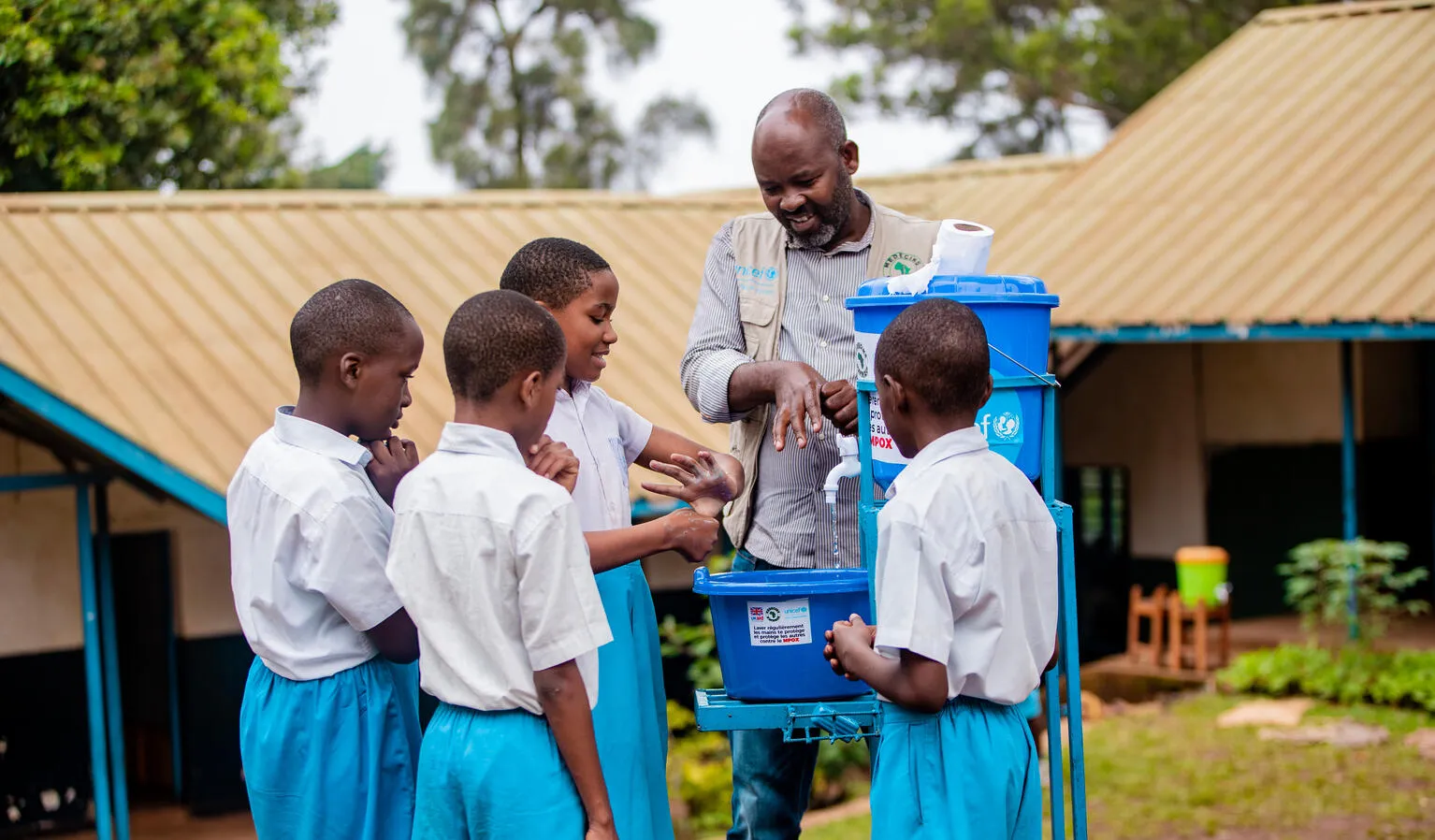 In a school courtyard, a health worker demonstrates proper handwashing to students.