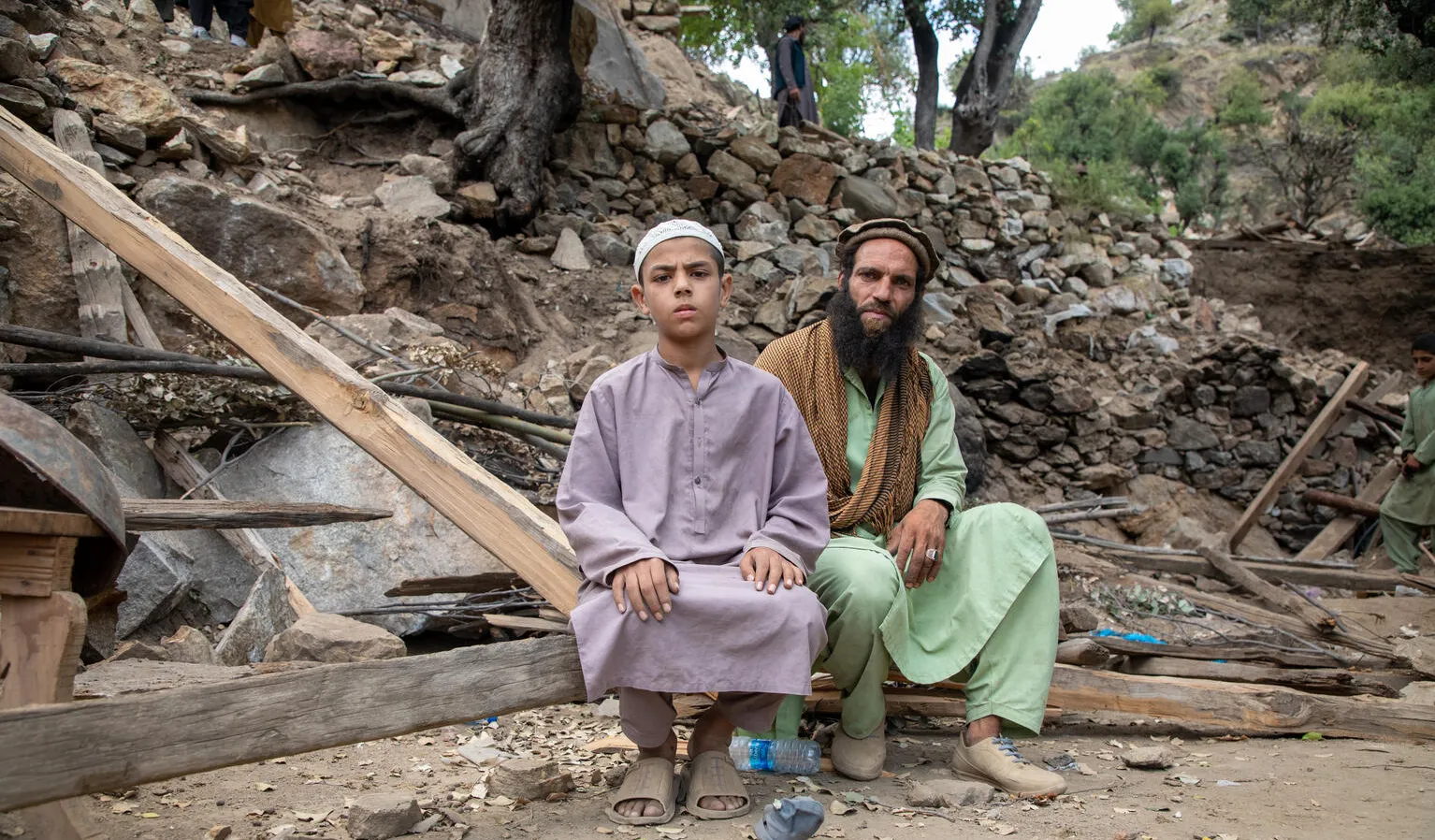 Un homme et un enfant sont assis devant des décombres.