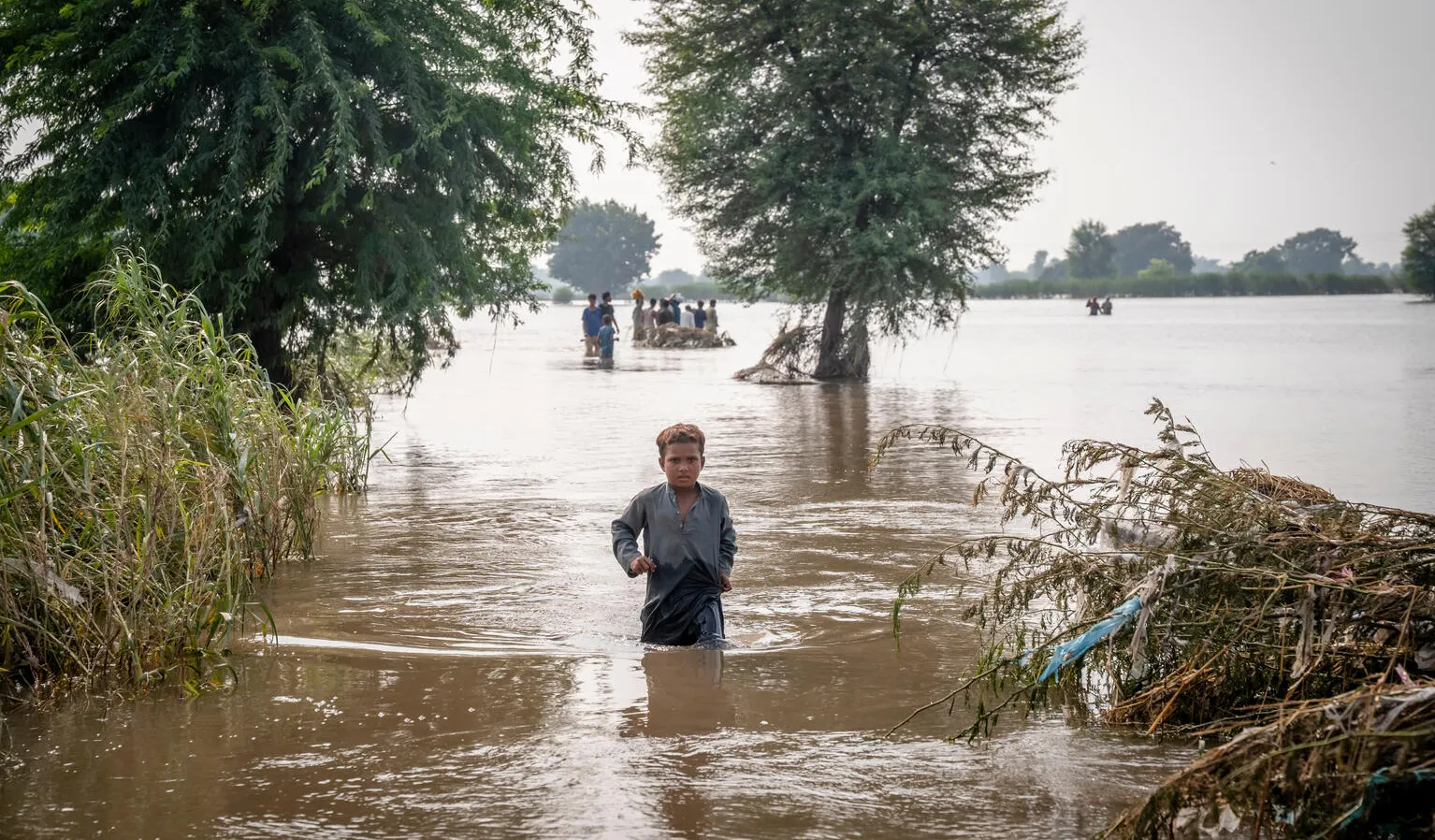 A boy walks across water in a flooded field.
