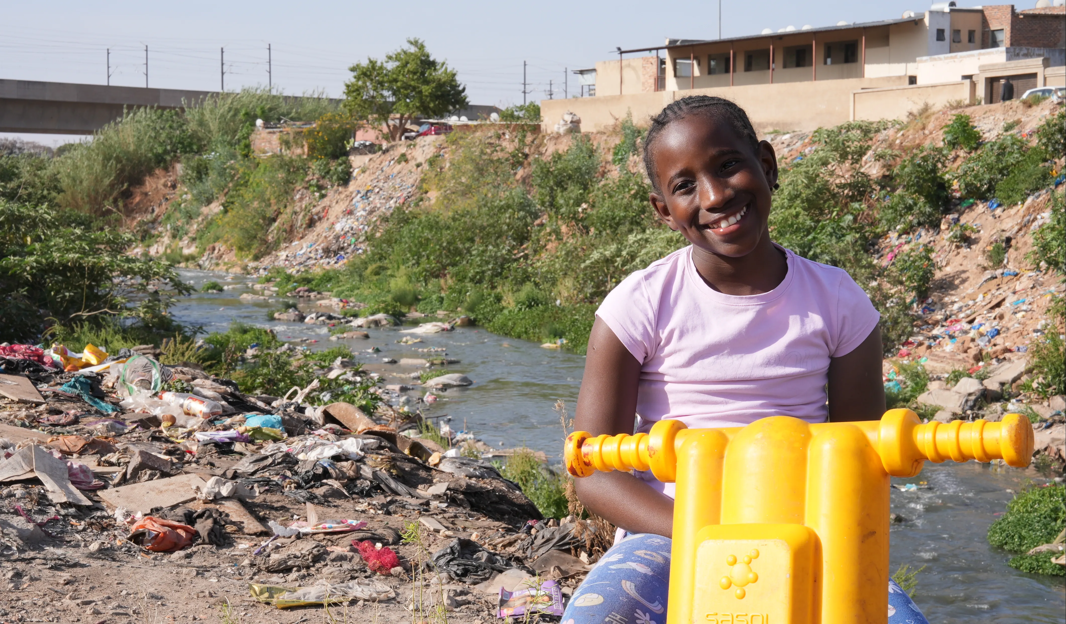 Le 16 septembre 2025 : Ompfuna, dix ans, roule en trottinette le long de la rivière polluée de Jukskei à Johannesburg, en Afrique du Sud.