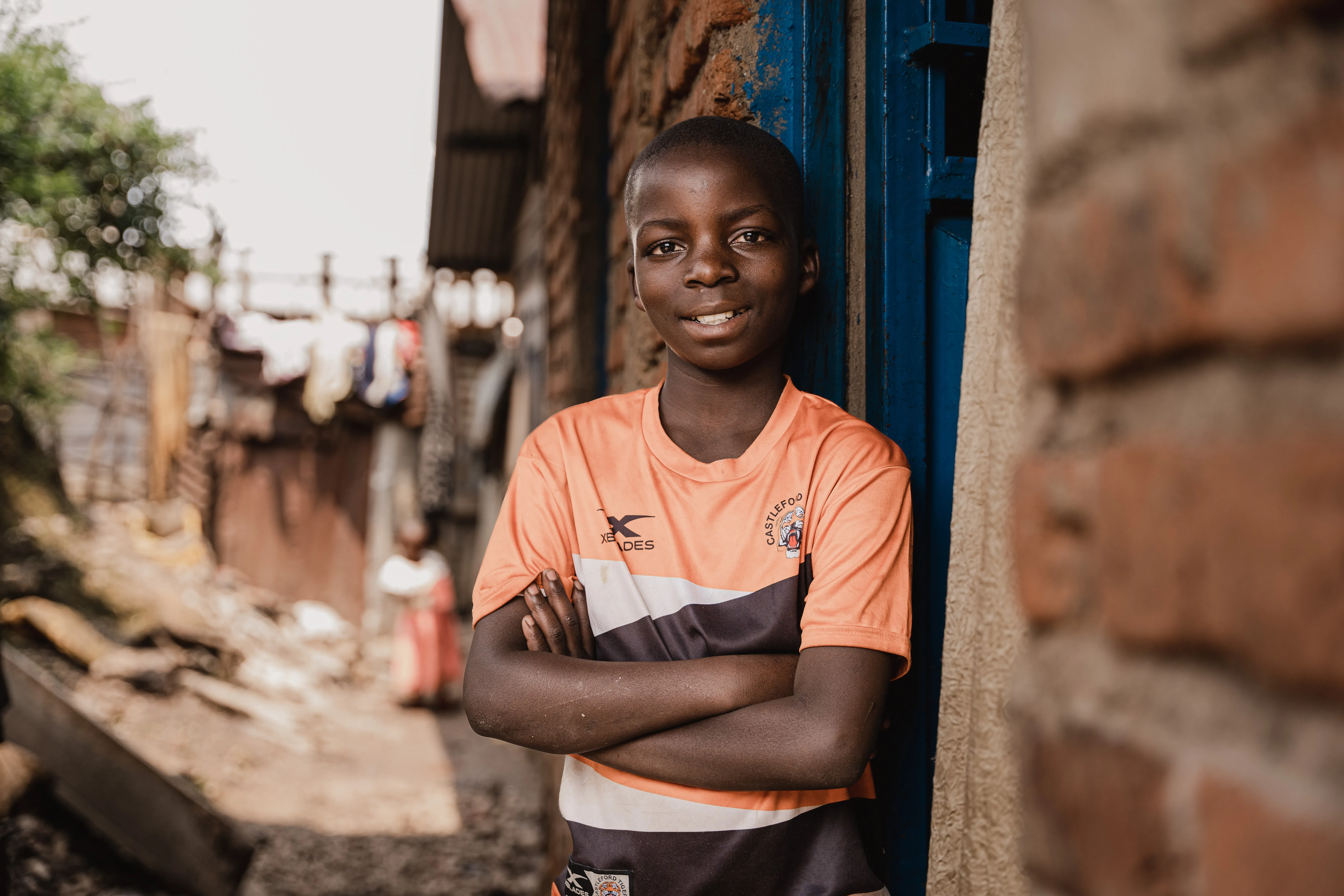 Boy with arms crossed standing in a doorway in a residential alley.