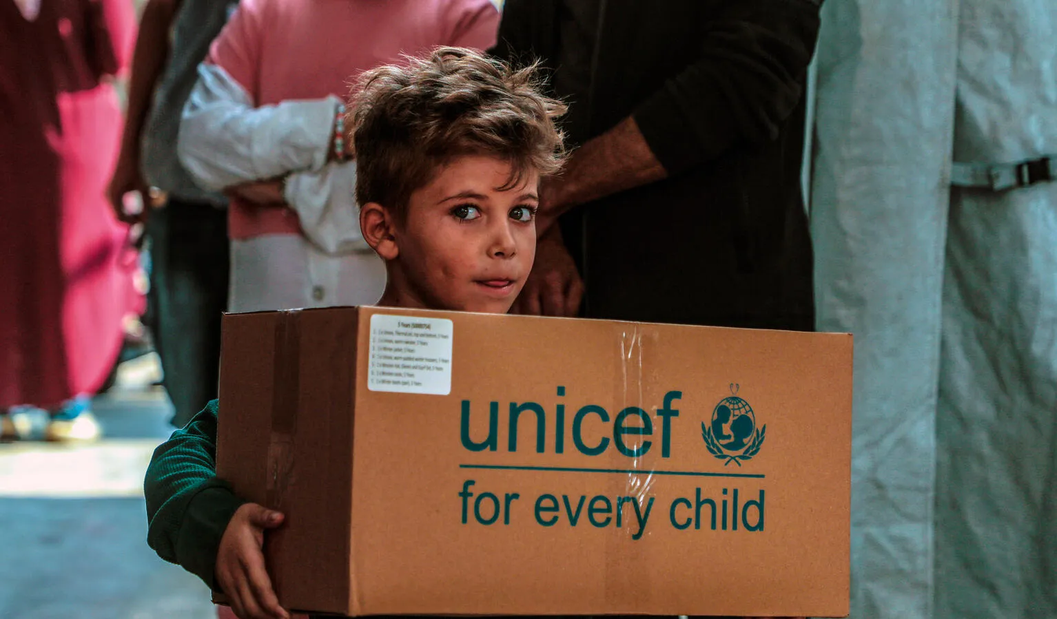 Un enfant portant une boîte au logo de l’UNICEF regarde l’objectif.