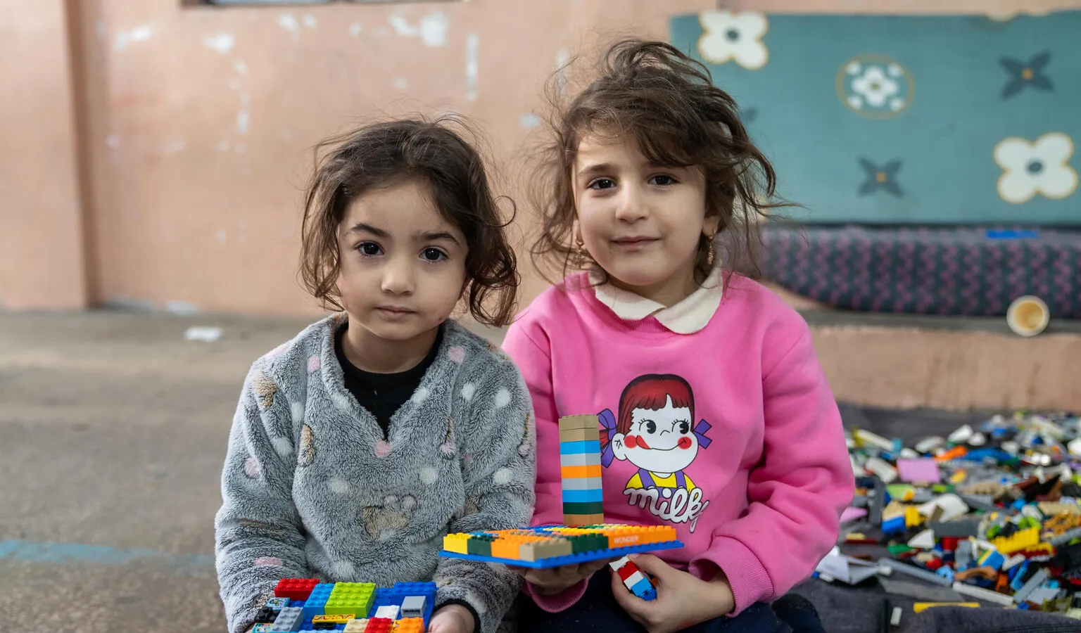 Dans un refuge, deux enfants assis par terre tiennent des créations Lego colorées.