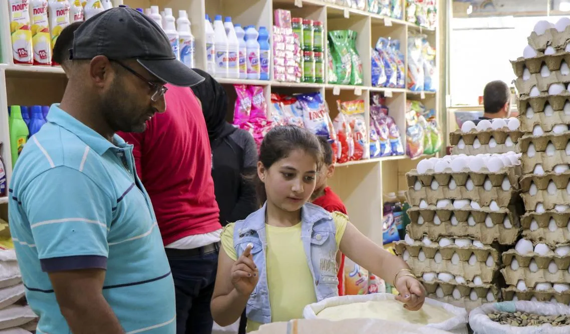 Lamis helps her father shop at a store in Aleppo.