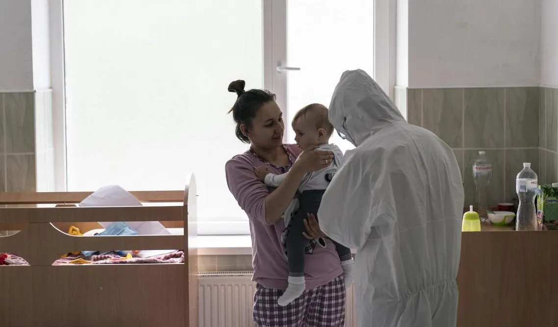A doctor checks a baby, being held by her mother.