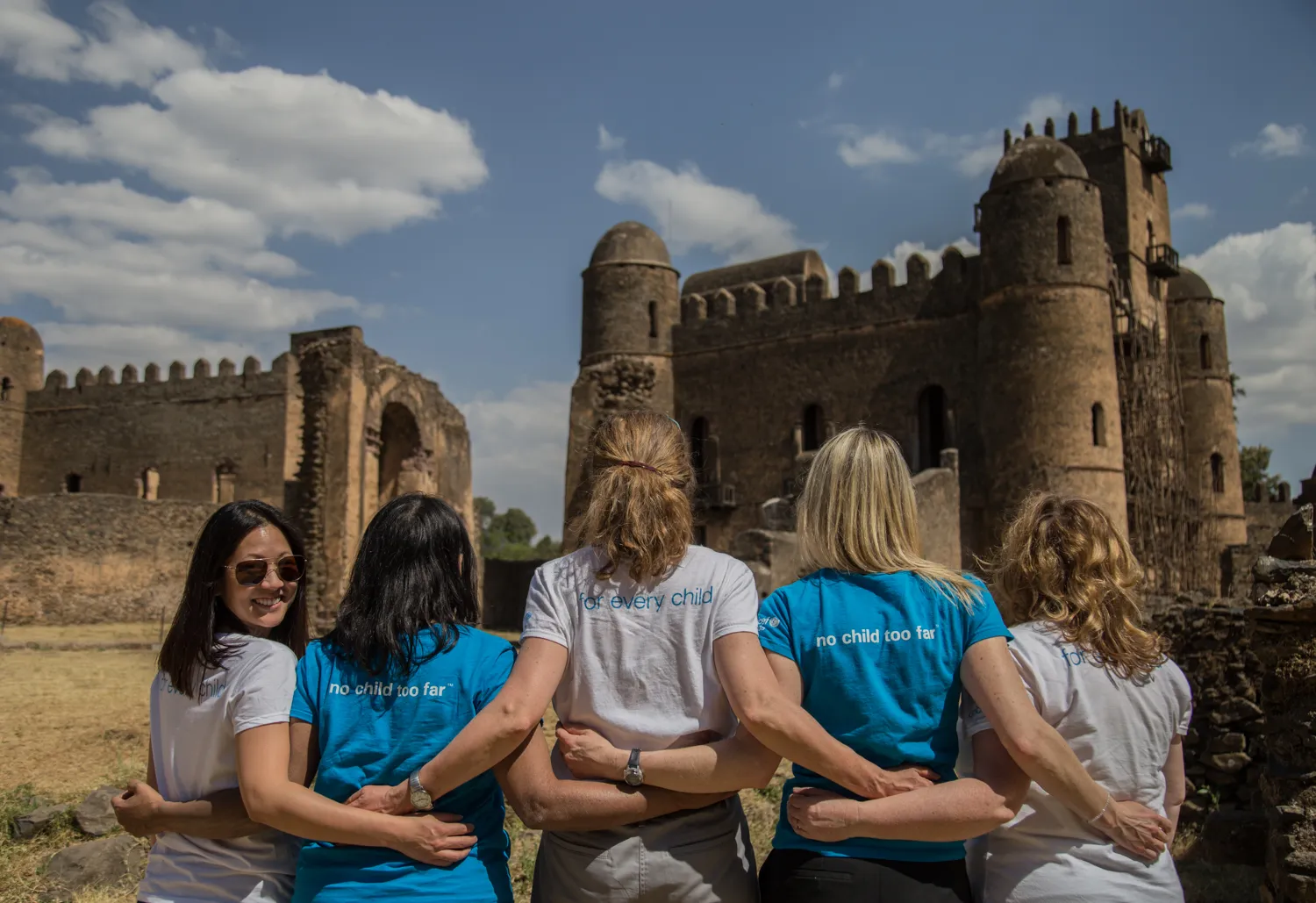 A group of five women stands in line, four facing forward while one turns to engage the camera.