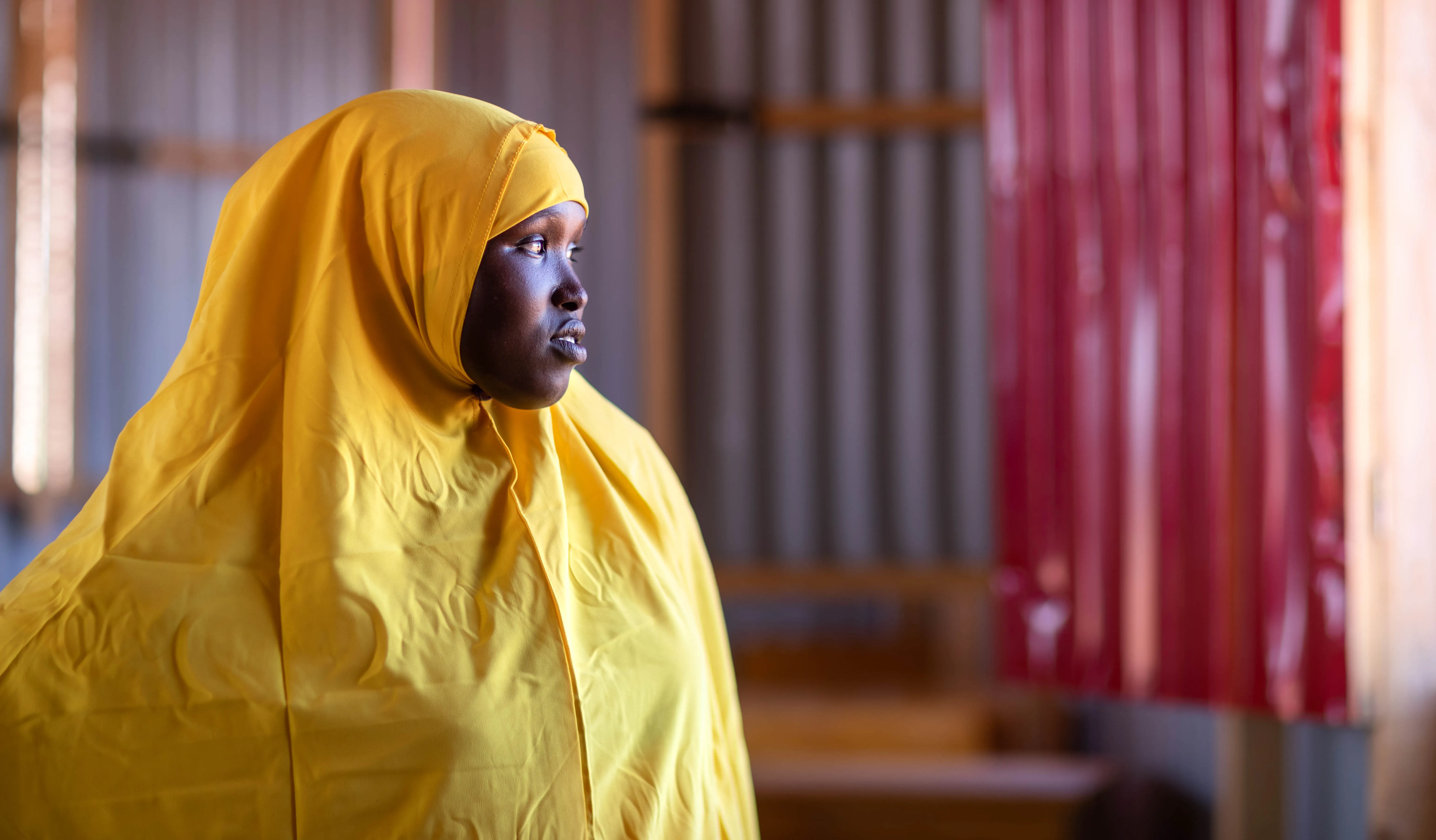 A girl wearing a yellow uniform with a yellow scarf stands by a door looking outside contemplatively. 
