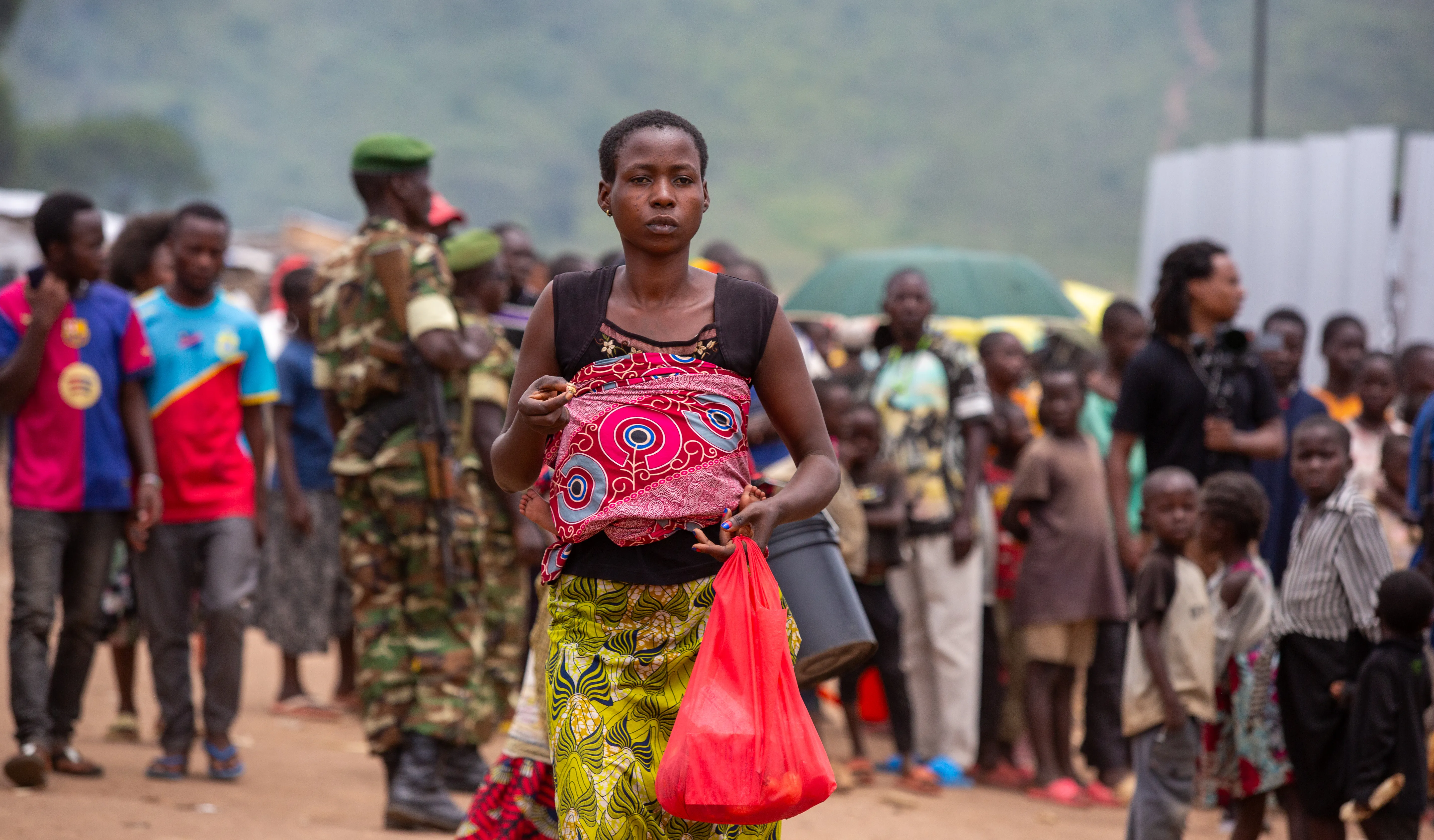 A woman carrying a baby walks through a crowded path    