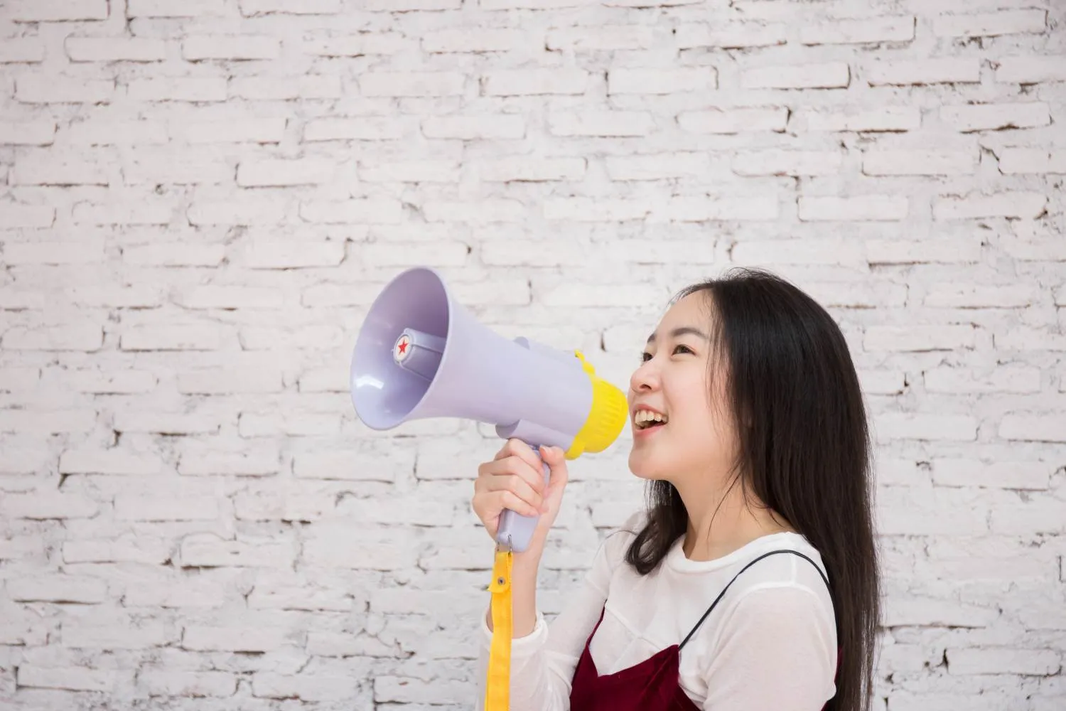 Smiling teen girl holding megaphone in front of a white brick wall