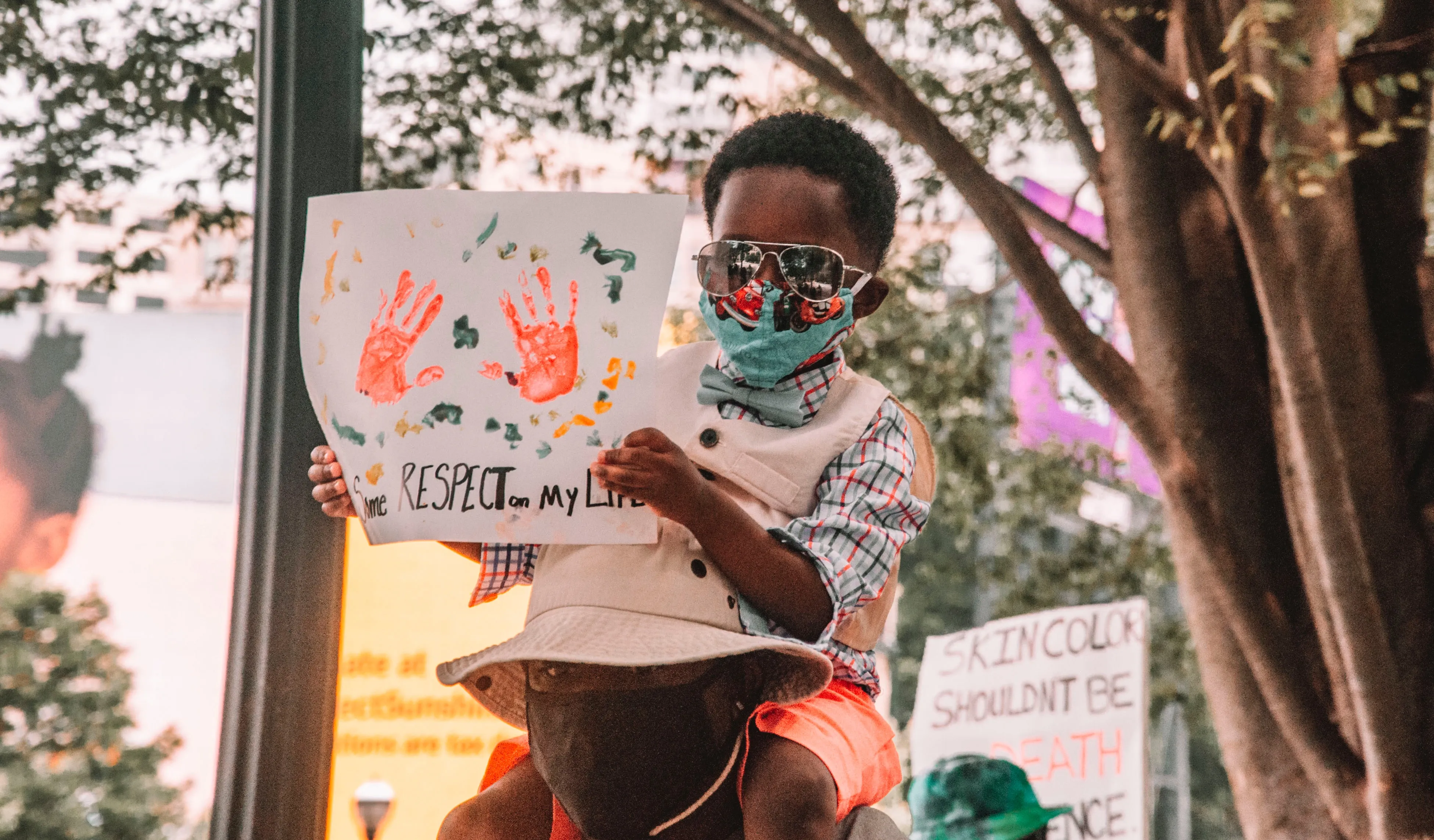 A child sits on a man's shoulders holding a protest sign.