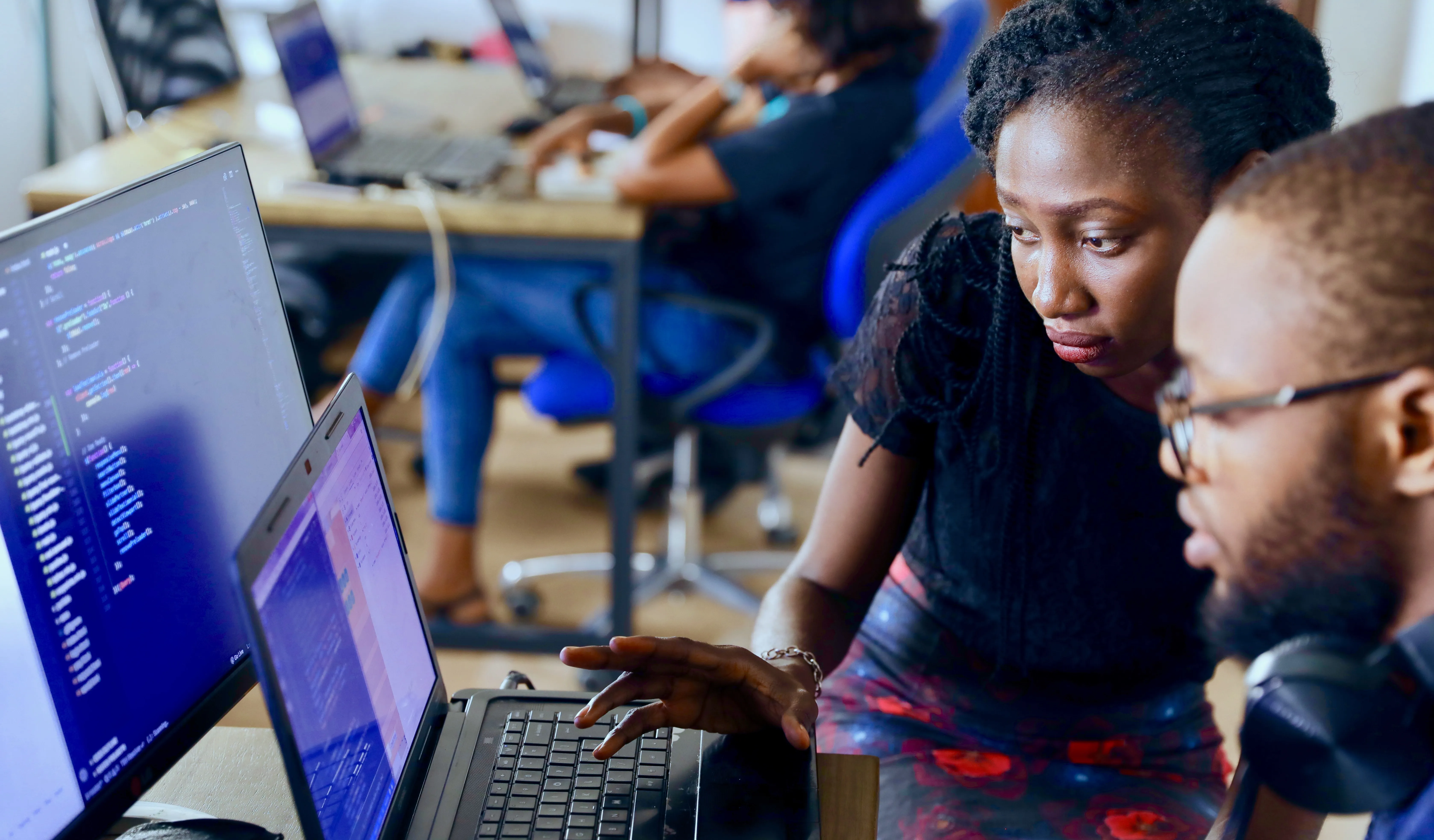 a man and a woman work at a computer which is showing code.