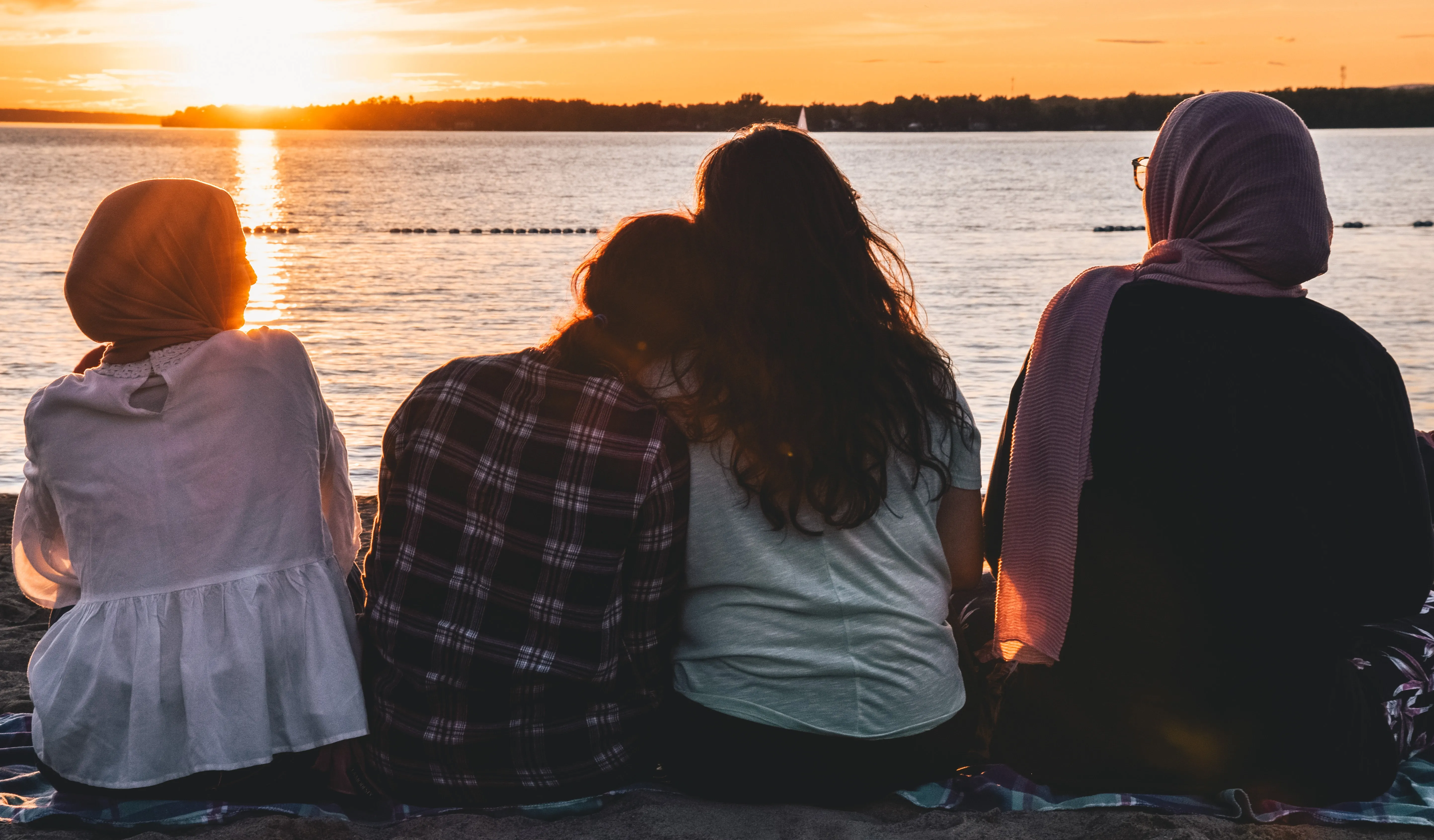A group of young girls sit facing a sunset.