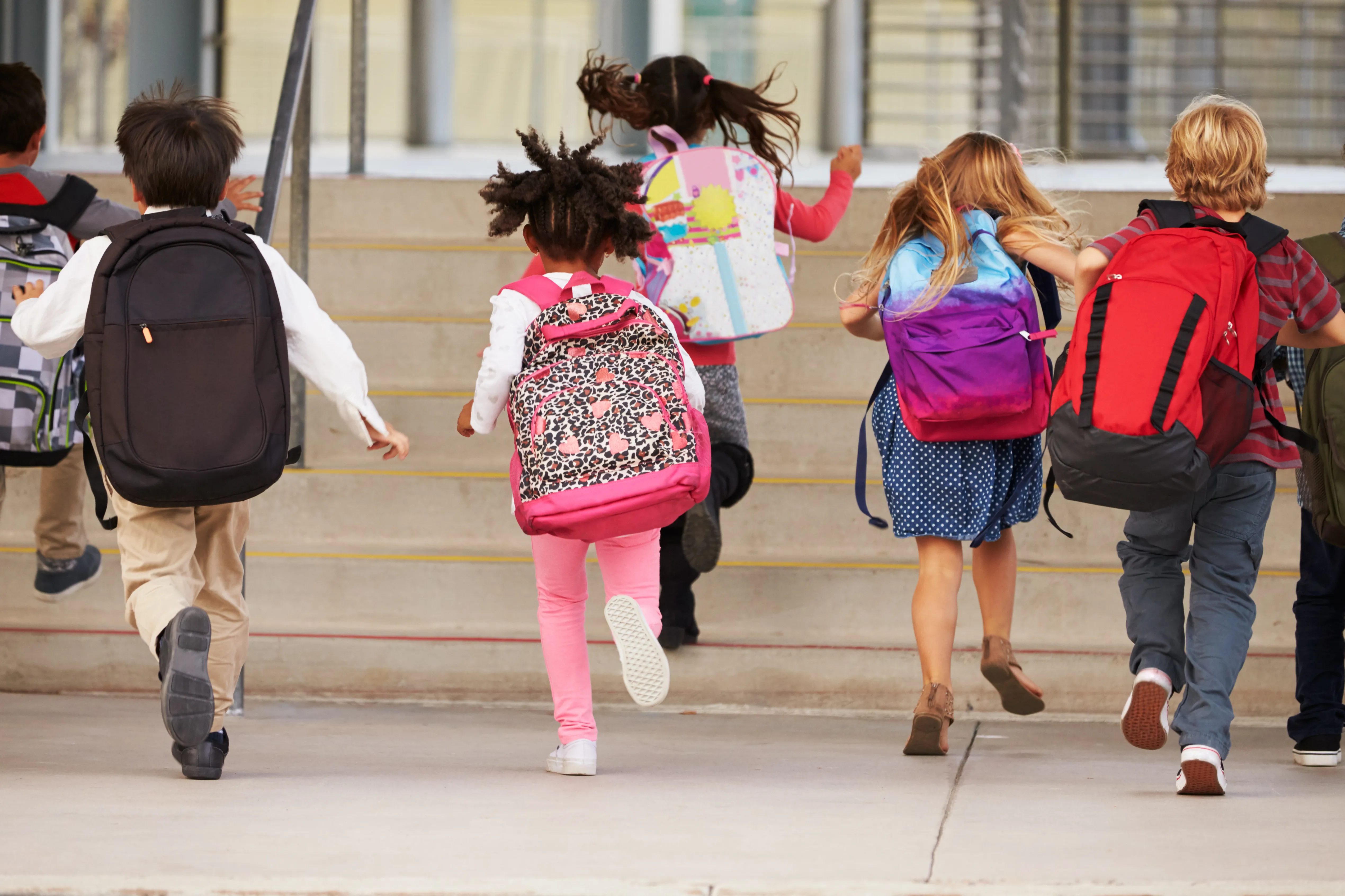 Kids wearing backpacks running into school