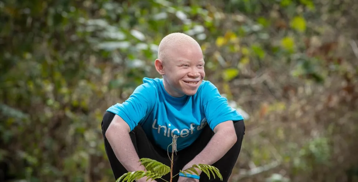 Emmanuel, a young climate advocate, plants a tree while wearing a blue UNICEF t-shirt.