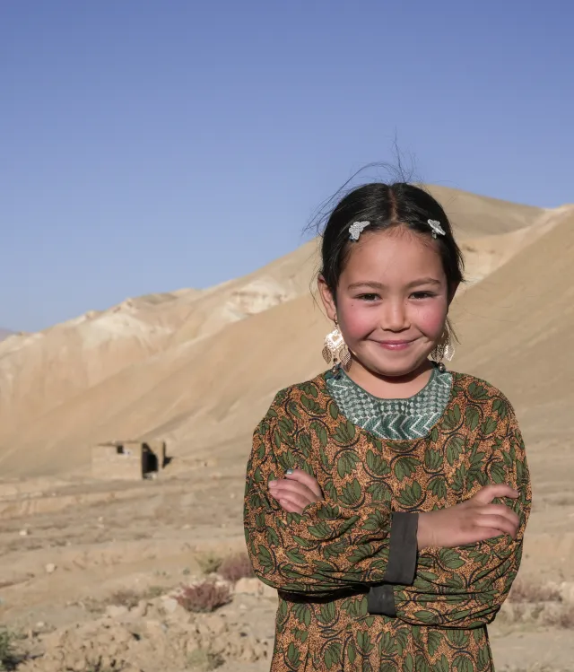 Girl with her arms crossed, smiling, standing on a hillside in rural Afghanistan.
